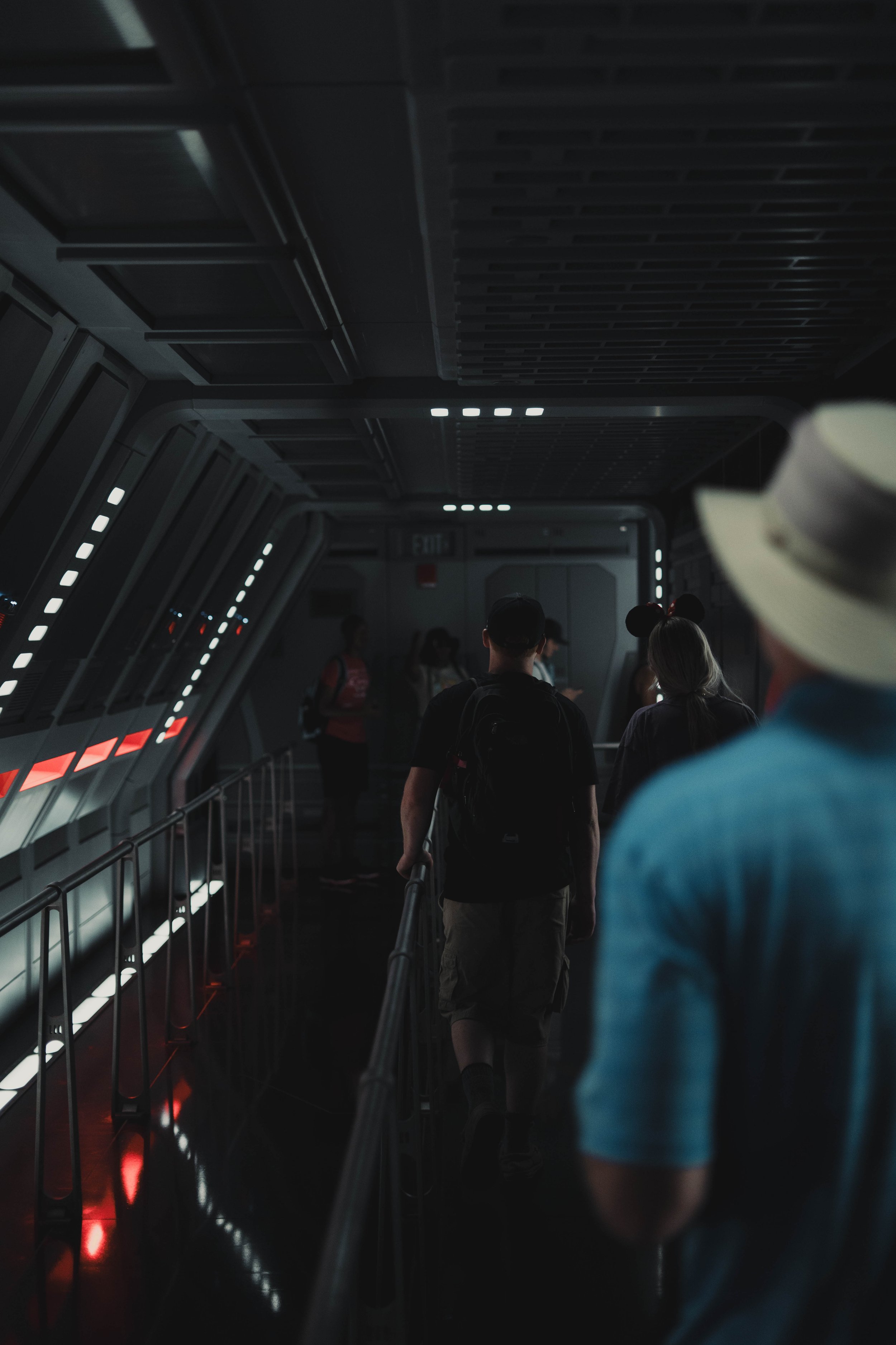 People walking in a dark, futuristic corridor with high-tech lighting.