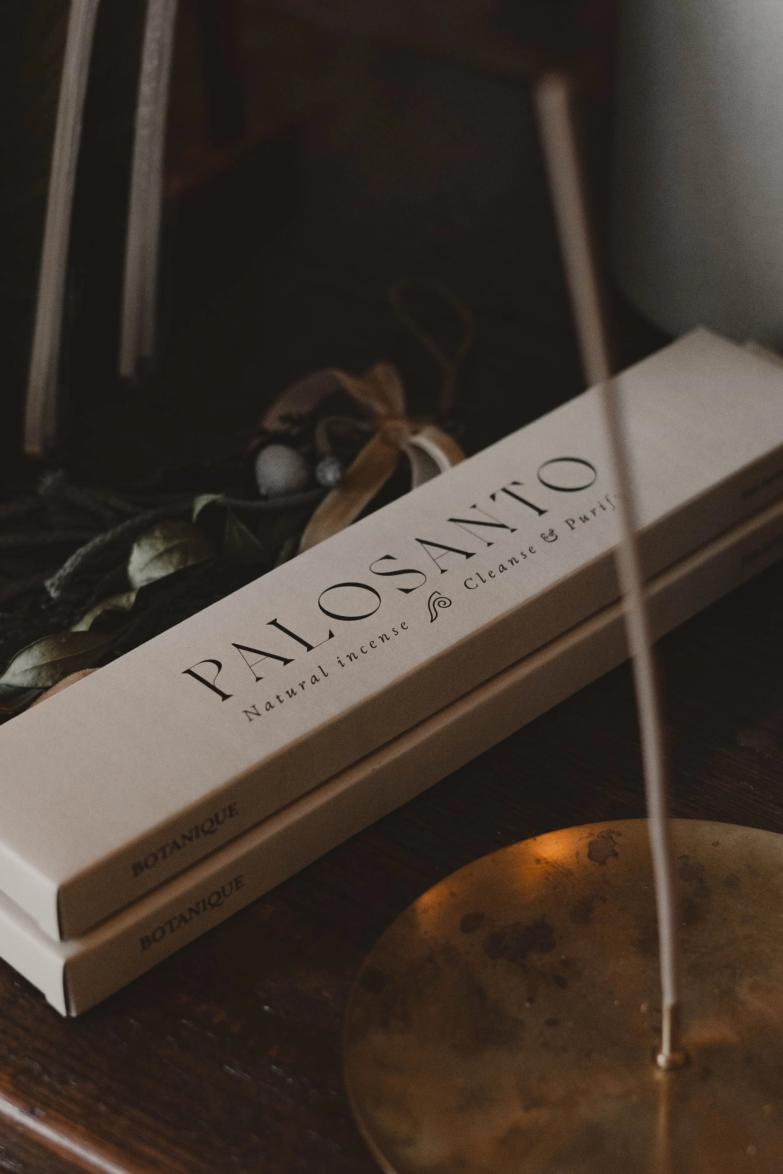 Box of Palo Santo natural incense sticks on a wooden surface with a decorative dried plant and blurred background.