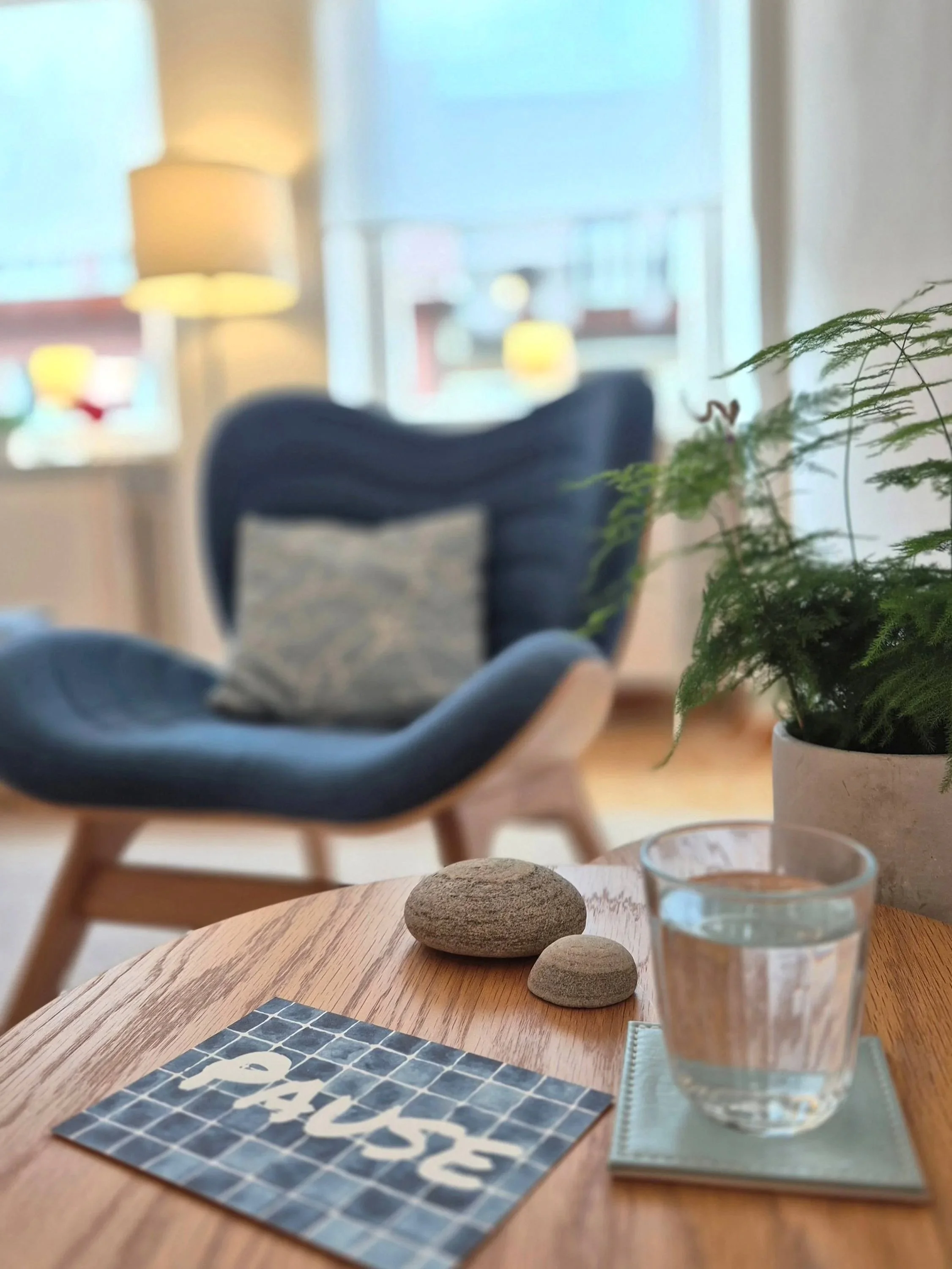 Eine Karte mit der Aufschrift "Pause", dahinter ein bequemer Sessel, freundliche, helle  Atmosphäre in einem Therapieraum