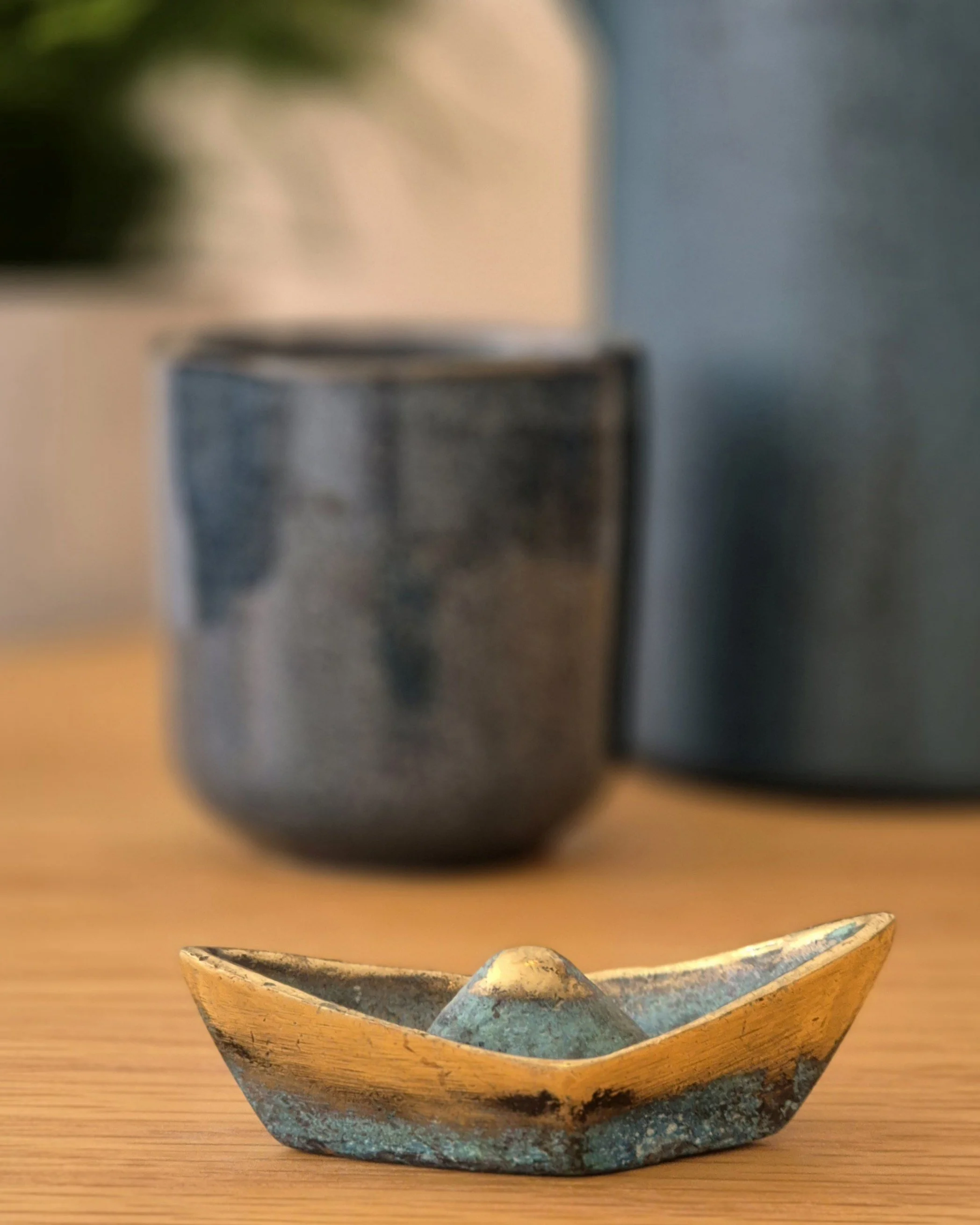 Eine Bronzeskulptur eines Fischerbootes, im Hintergrund eine Teetasse - Symbol für Stabilität und Sicherheit in schwierigen Zeiten