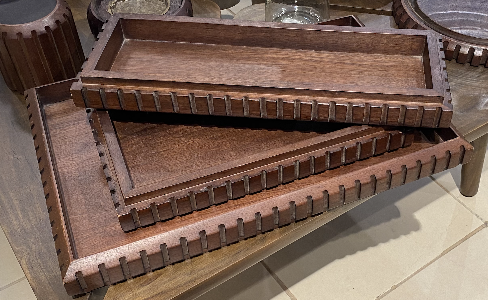 Stack of three rectangular wooden trays with slotted edges, placed on a wooden table.