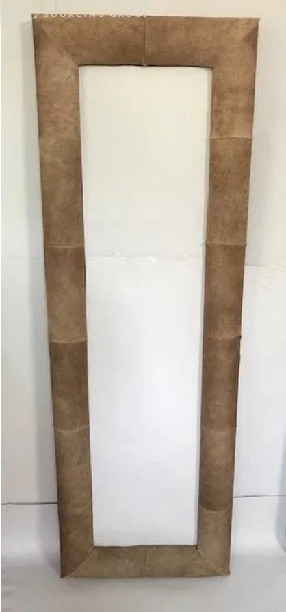 A rectangular mirror with a frame made of brown tiles, positioned vertically against a white tiled wall.