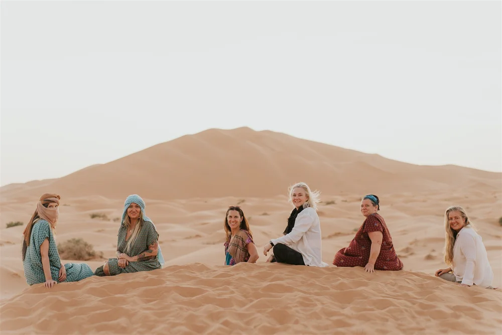 Retreat travelers resting together on the Sahara dunes on a Morocco yoga retreat