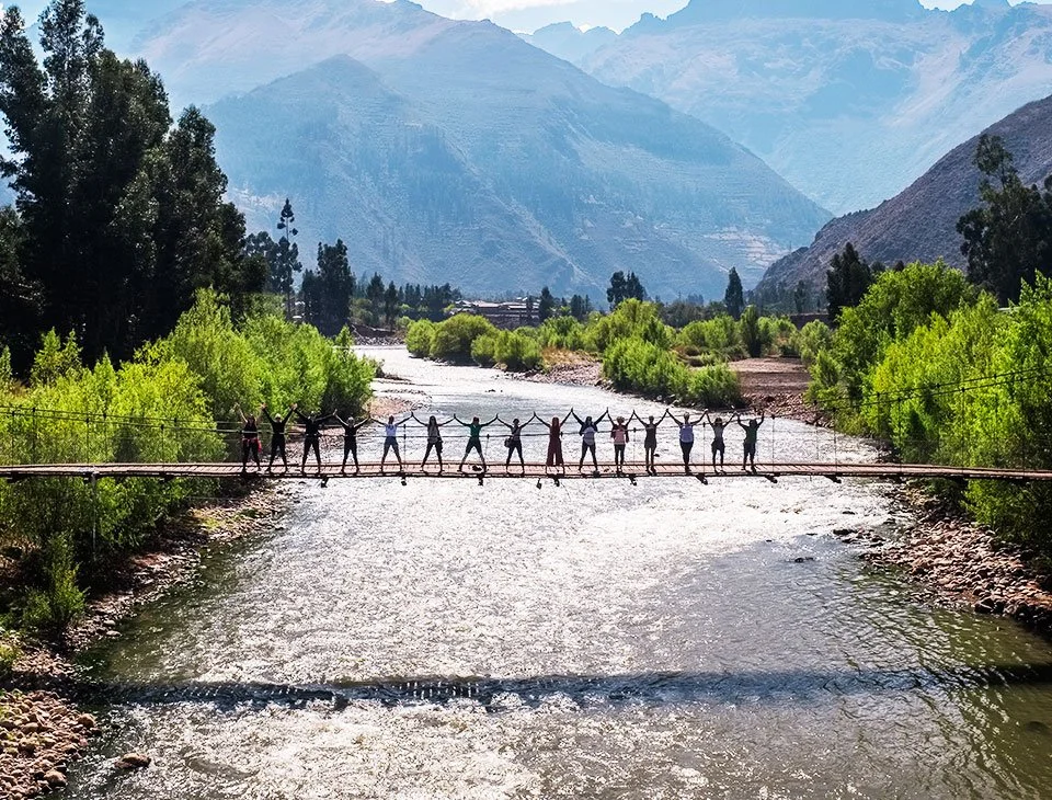 Women's yoga retreat group joining hands on a footbridge over a river in Peru's Sacred Valley