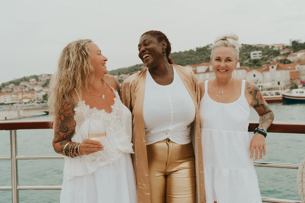 Three women laughing together on the deck of a yacht on a DDY Travels yoga retreat in Croatia