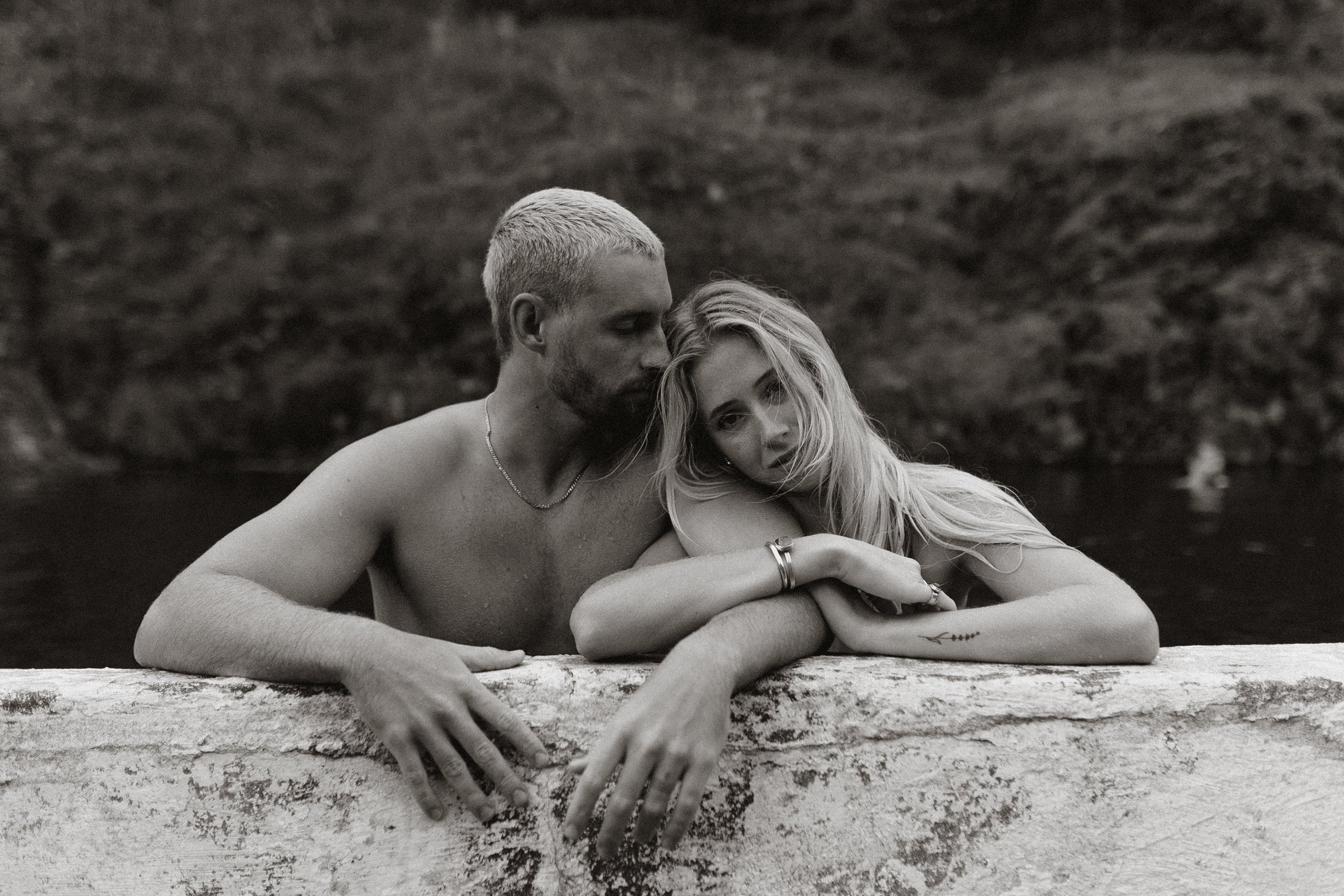 couple lean against the side of a wild swimming pool, having their engagement photos taken in rural Iceland