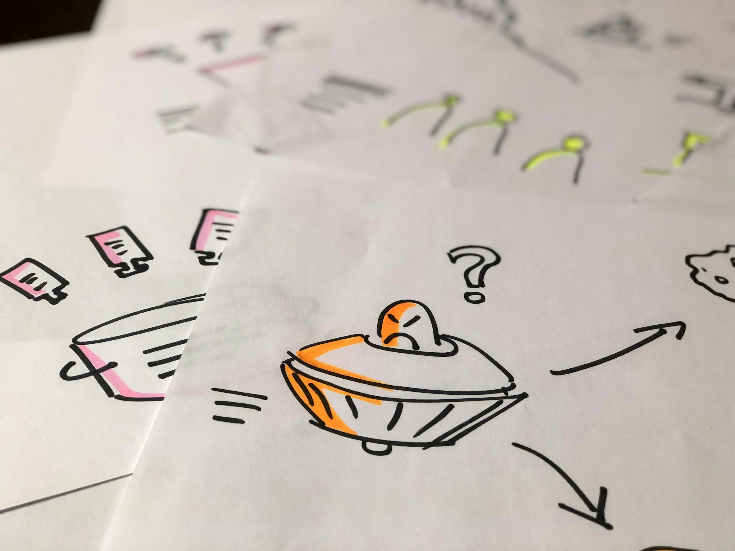 Hand-drawn sketches on paper, featuring abstract designs of a UFO with an alien, arrows, and colorful accents.