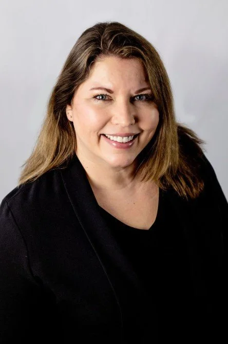Smiling woman in black jacket with long brown hair.