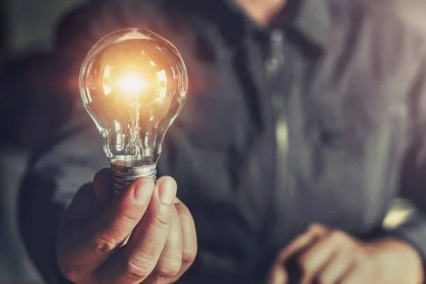 Person holding a glowing light bulb, close-up view.