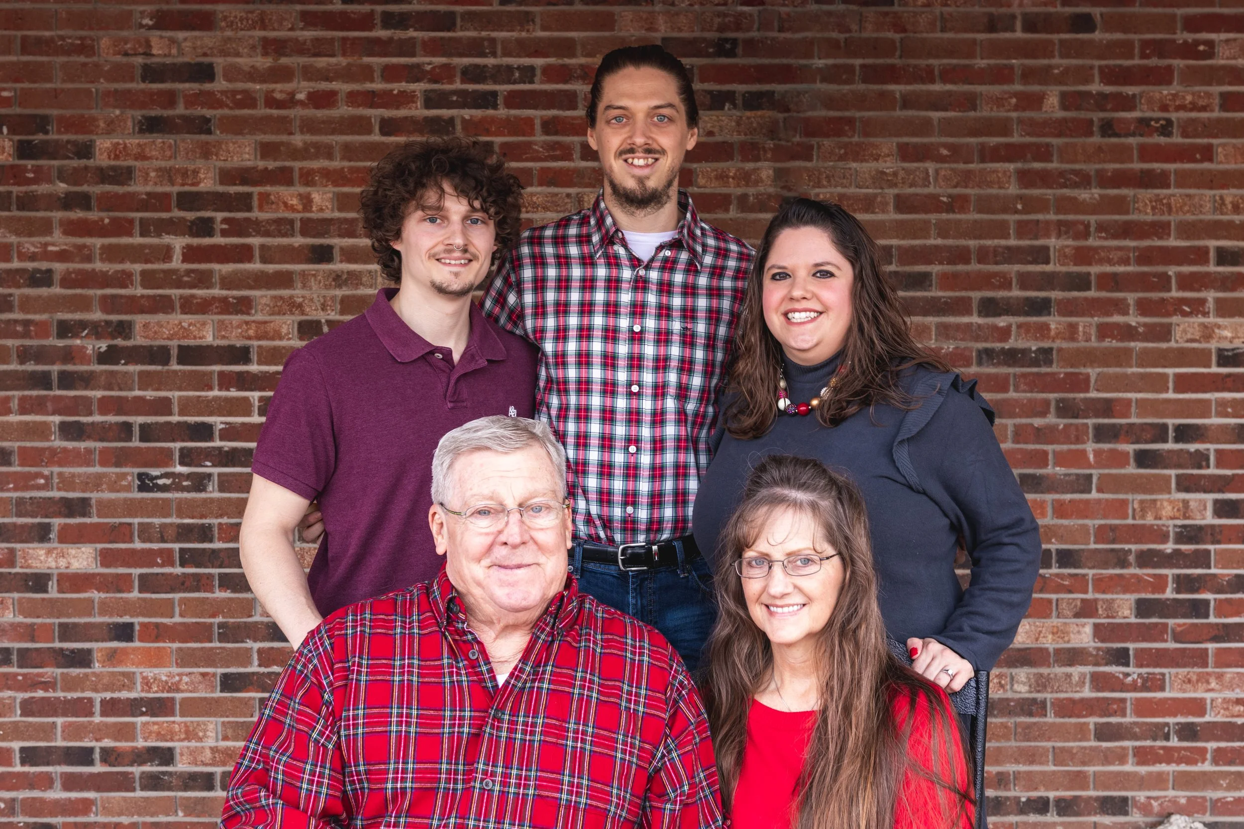 Family of six posing in front of a brick wall, with three men and three women, all smiling.