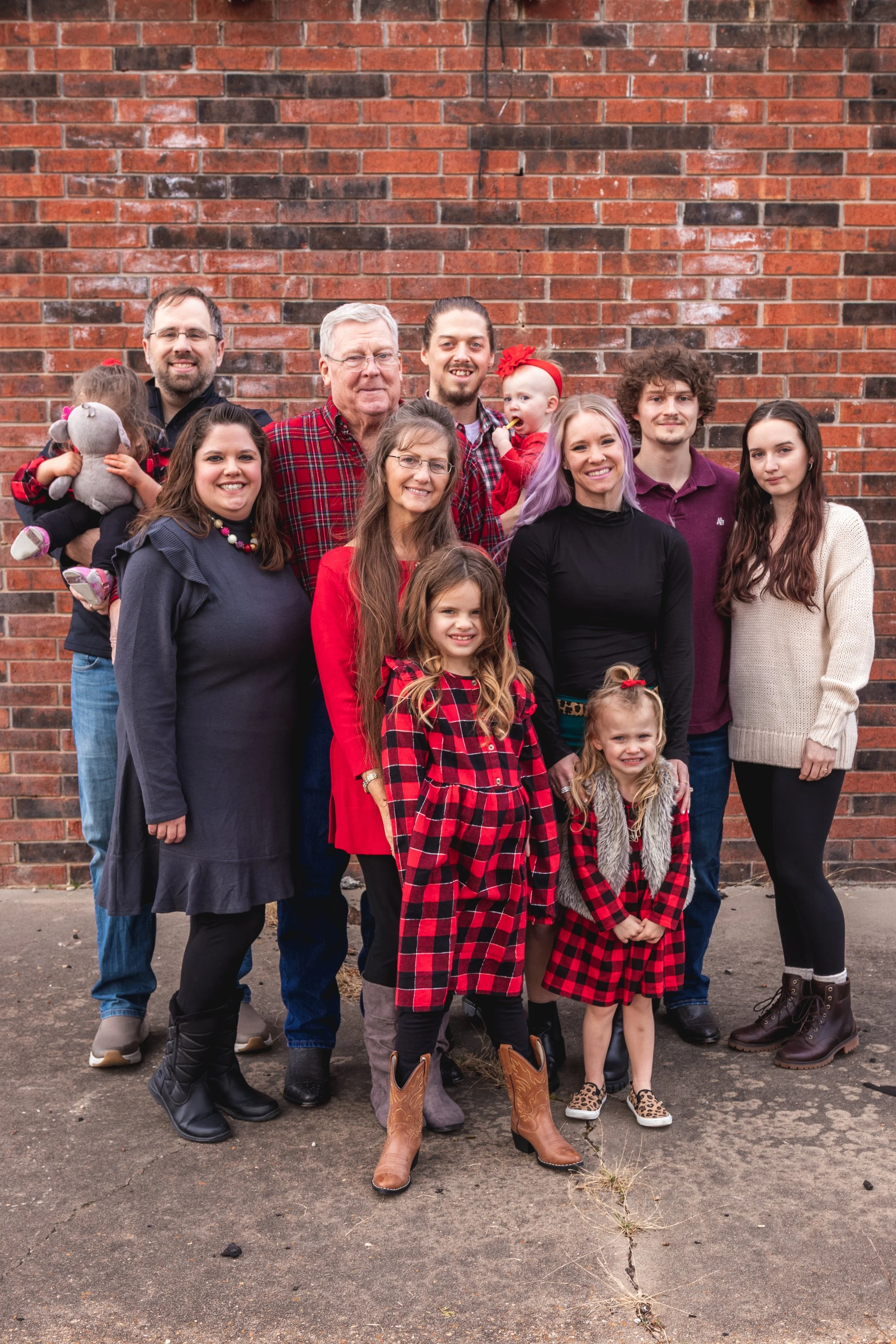 Family group standing in front of a brick wall, dressed in casual and festive clothing.