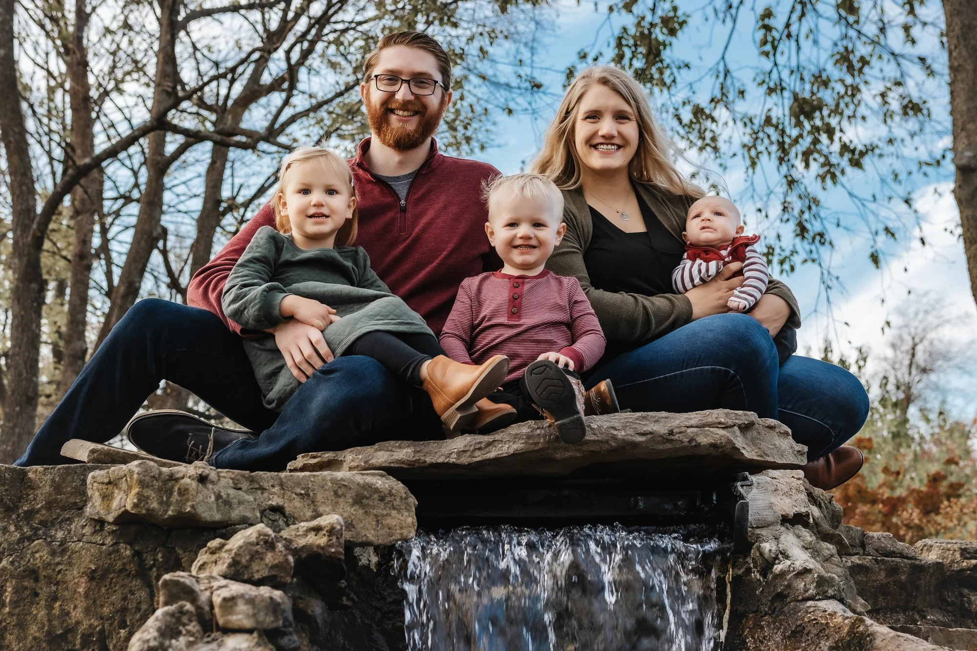 family of four posing on rocks of waterfall at nathanael greene in springfield mo