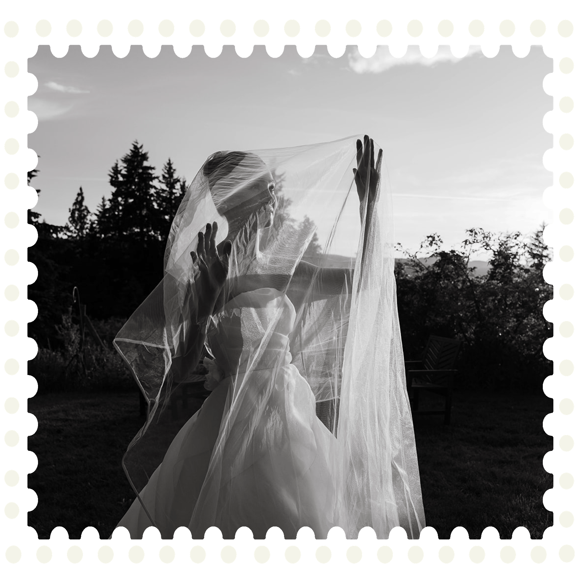 A woman in a wedding dress with a veil is standing outdoors, with trees and a cloudy sky in the background, holding or adjusting her veil.