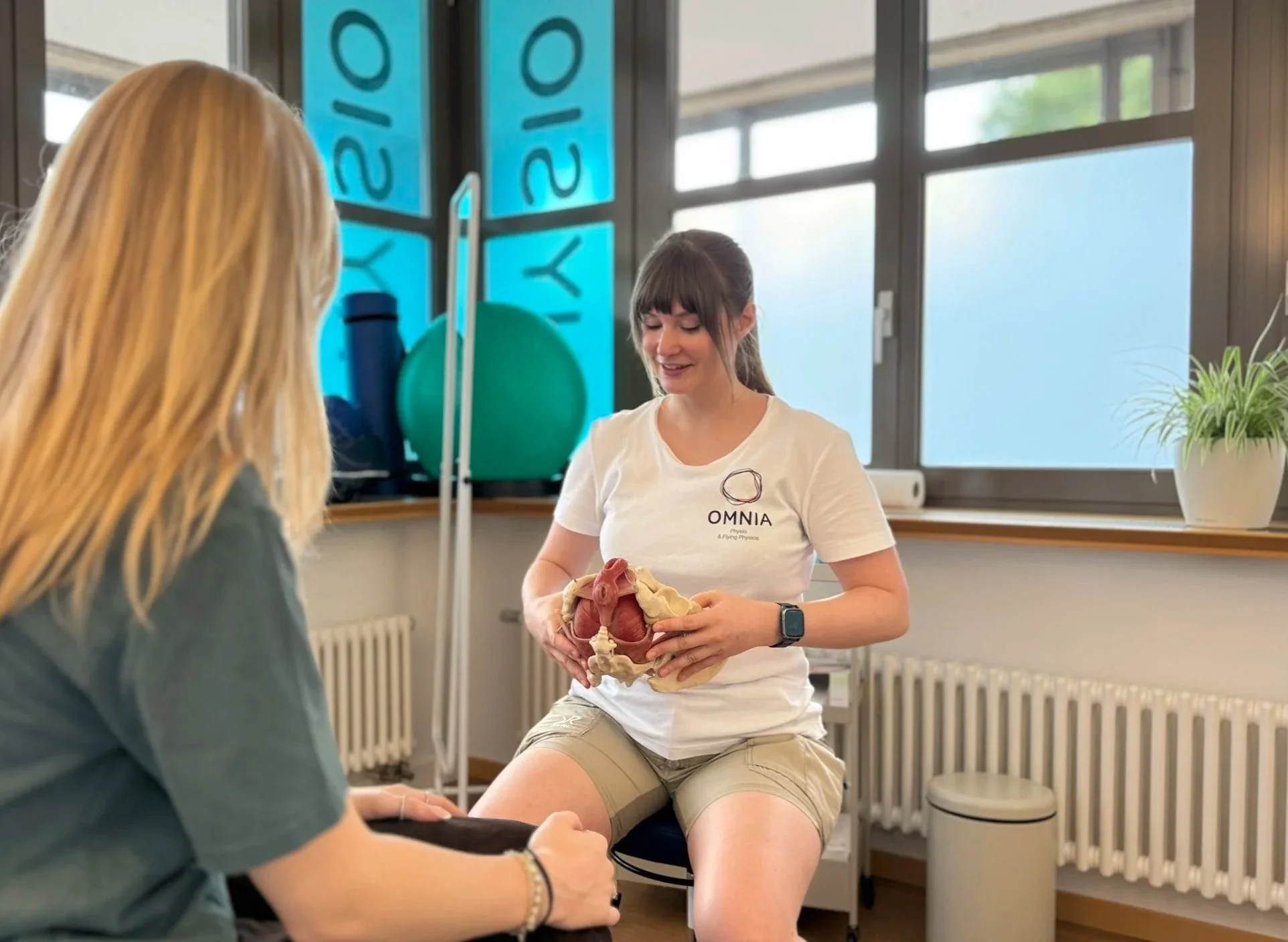 Physiotherapeutin von OMNIA Physio erklärt einer Patientin den Beckenboden am Beckenmodell