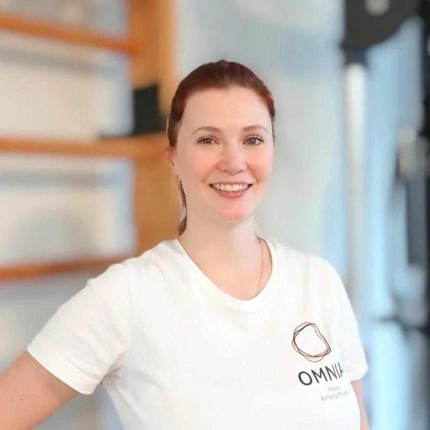 Lächelnde Frau mit roten Haaren in weißem T-Shirt, im Hintergrund eine helle, moderne Küchenszene.