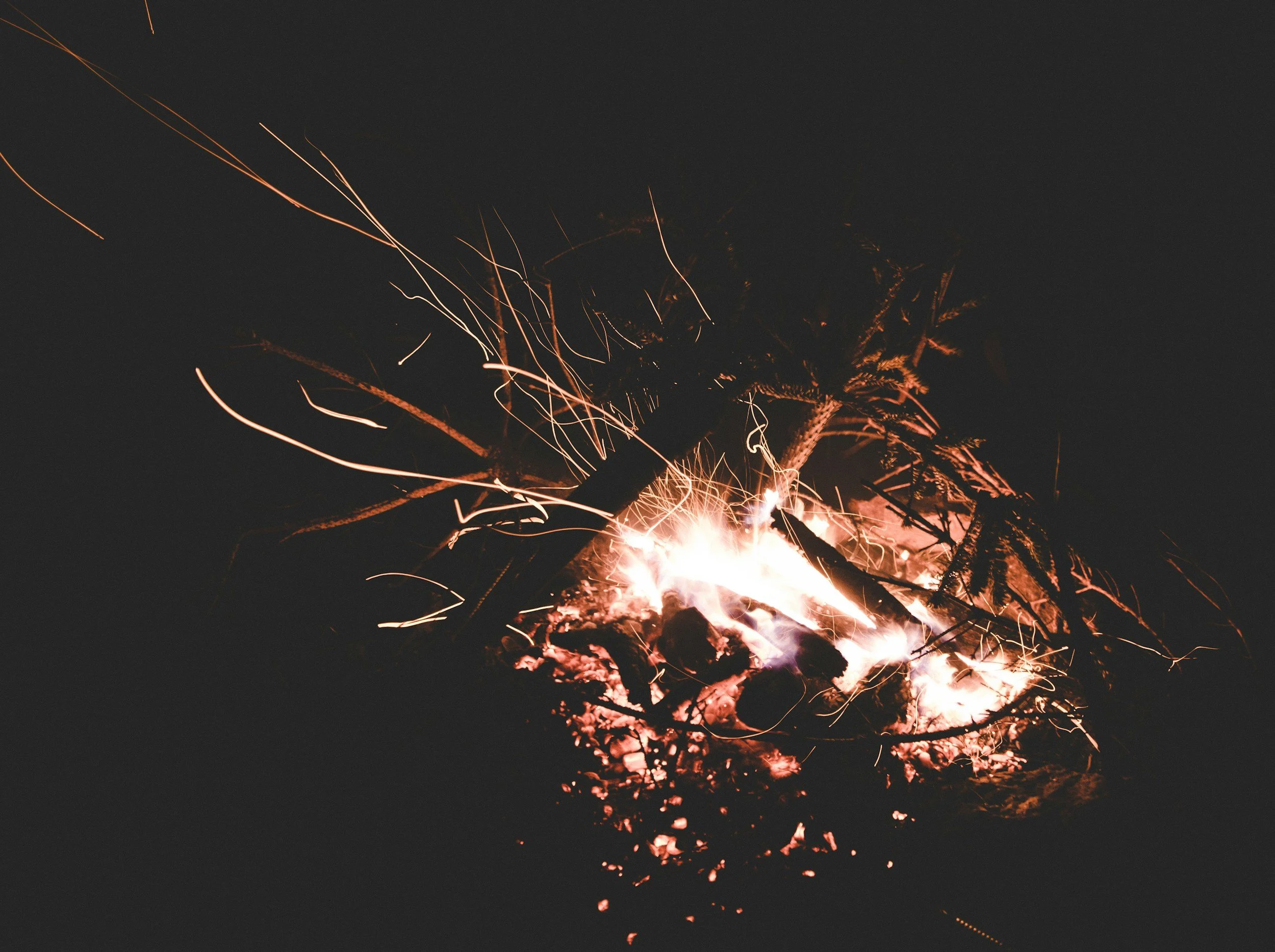 Falling burning logs and branches with sparks and embers in a campfire during the night.