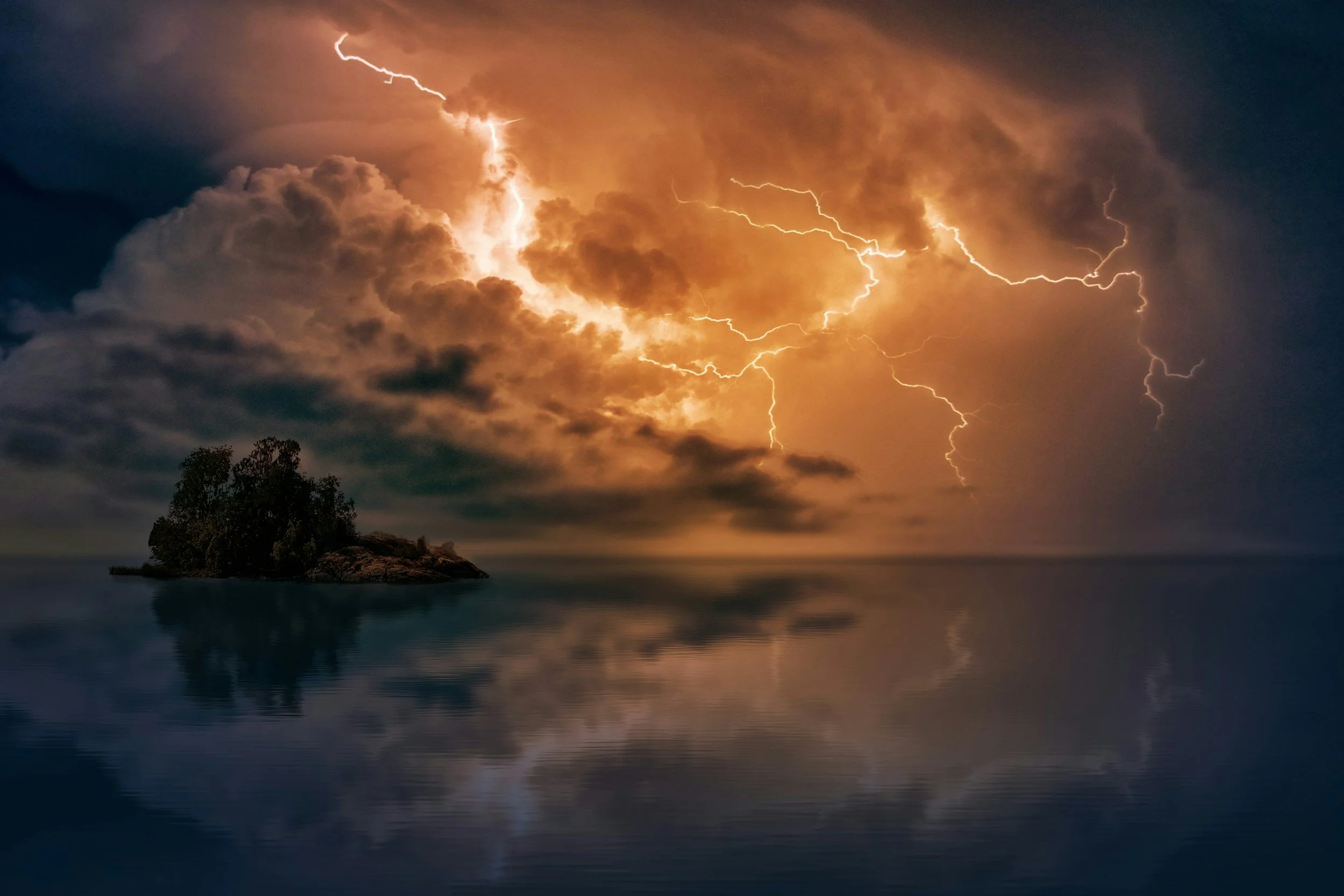Stormy sky with lightning over a small island surrounded by calm water, with reflections of the thunderstorm in the water.