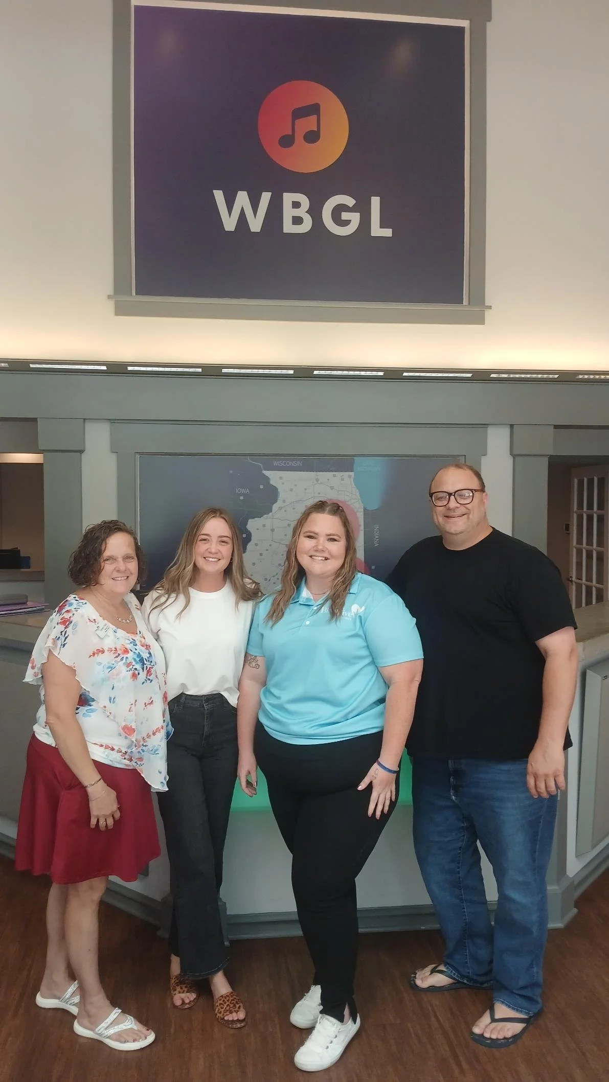 Photo of four adults standing and smiling at the camera. Pictured are 3 members of the Birth to Five Illinois Team and one person from the radio station.
