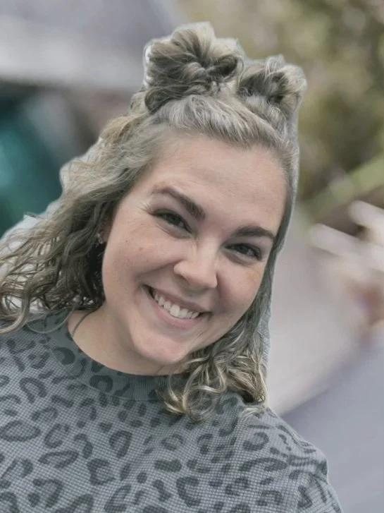 A light skinned woman smiling at the camera with a leopard patterned sweatshirt.