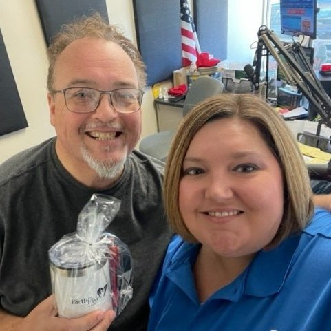 Pictured from left to right are a radio host and Liz Gibson. The radio host is holding a white Birth to Five Illinois branded tumbler cup while smiling.