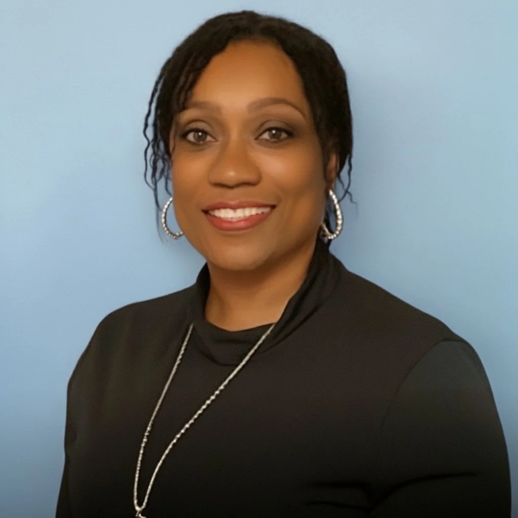 Photo of Cassandra Lee, a dark-skinned person with black hair. Cassandra is wearing a black top and a silver necklace with matching silver hoop earrings.