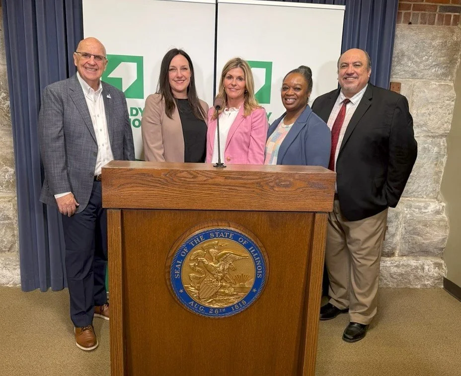 Image of five adults standing at a podium. See the description below the photo for the names and job titles of the individuals in the photo.
