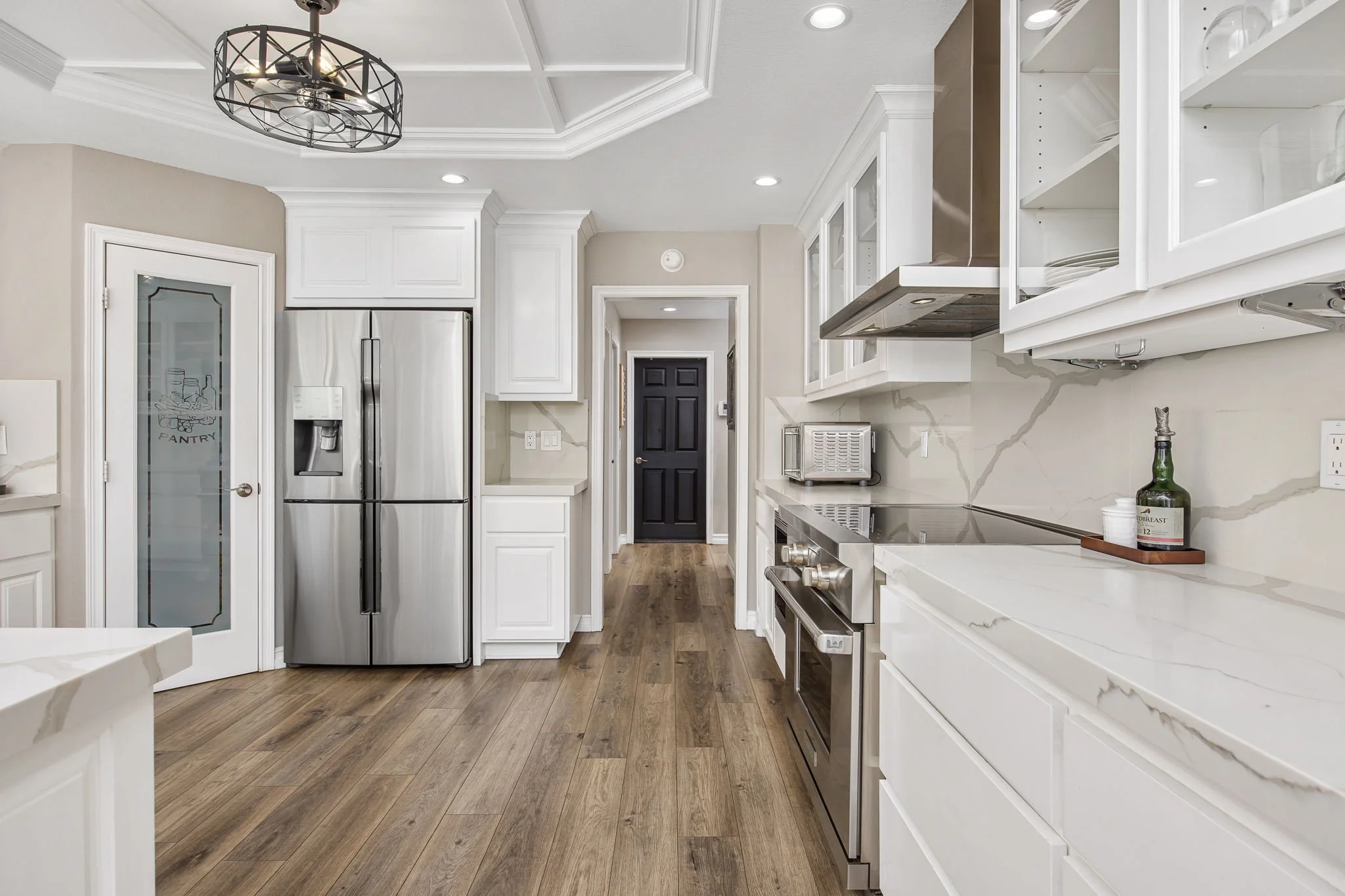Modern kitchen with white cabinets, stainless steel appliances, marble countertops, wooden flooring, and a black chandelier