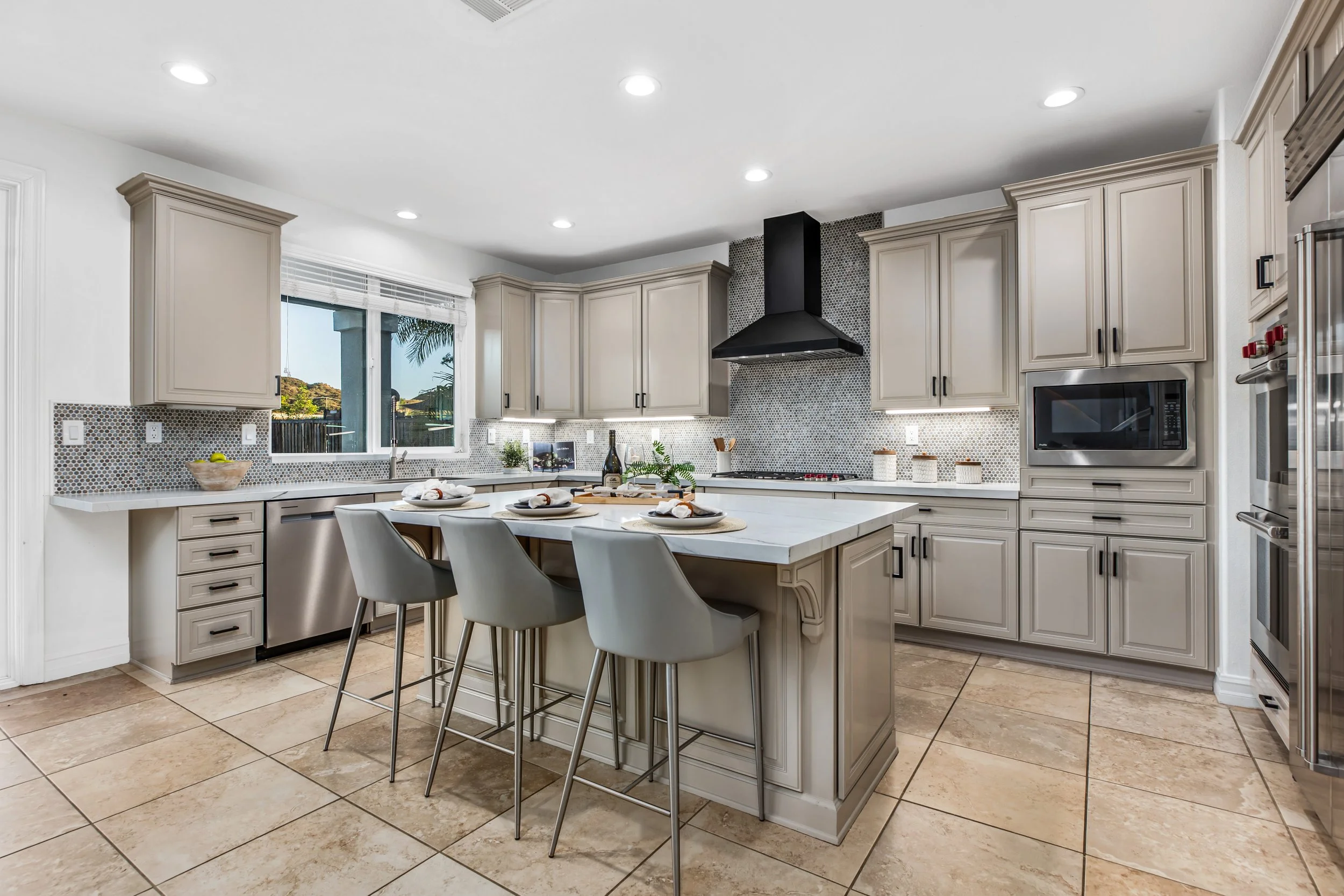 Modern kitchen with white cabinets, black appliances, and a island with four chairs, a window with blinds, and a black range hood.