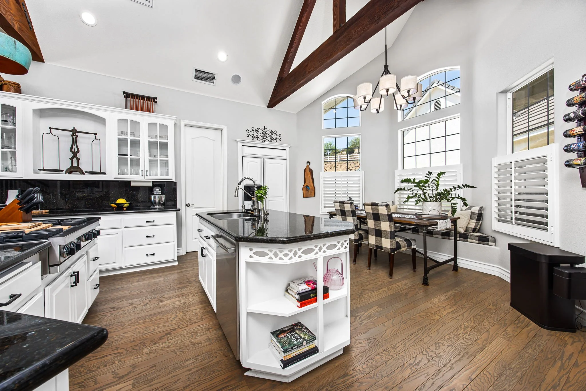 Bright, modern kitchen with white cabinetry, black countertops, a kitchen island, large arched windows, and a dining area with checkered chairs.