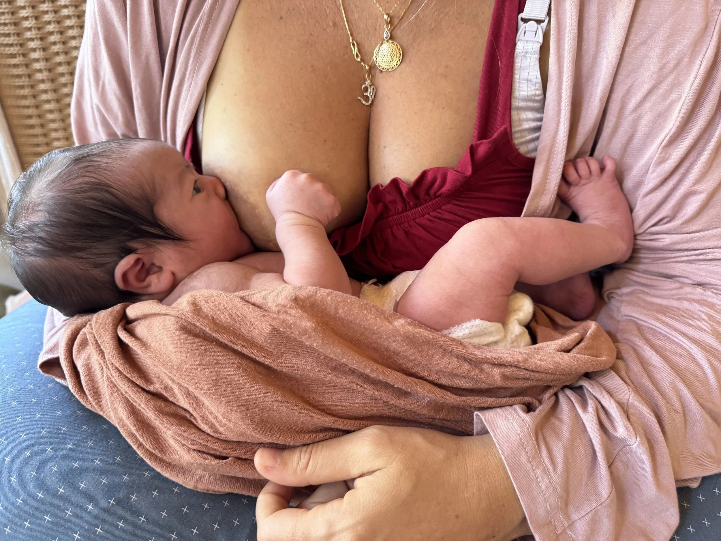 A baby is nursing from a woman's breast while lying on her lap.