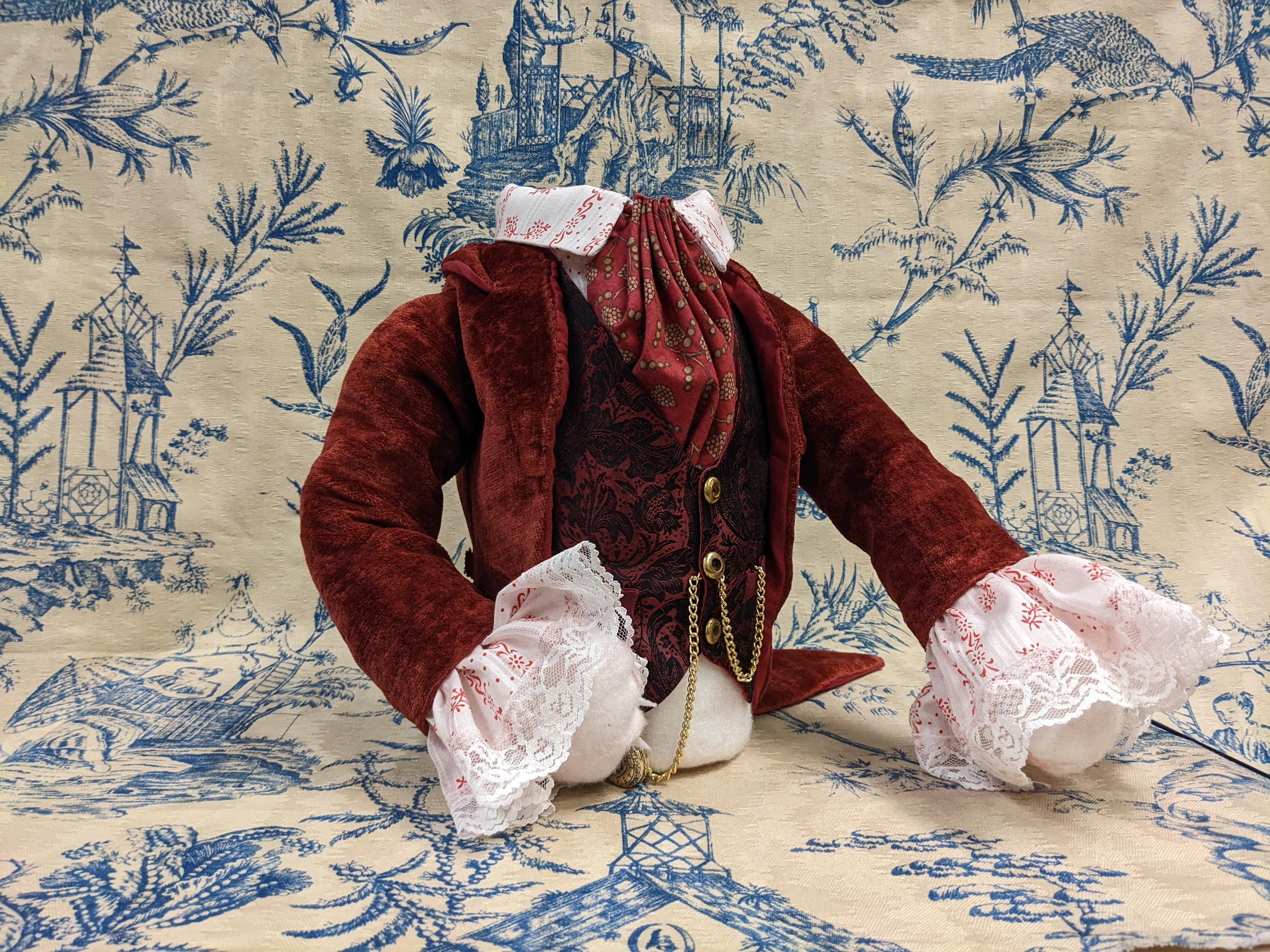 The body features a false waistcoat, false sleeve cuffs and jabot, a cravat, and a tailcoat. There are false coats on the waistcoat and the tailcoat, and it holds his watch.