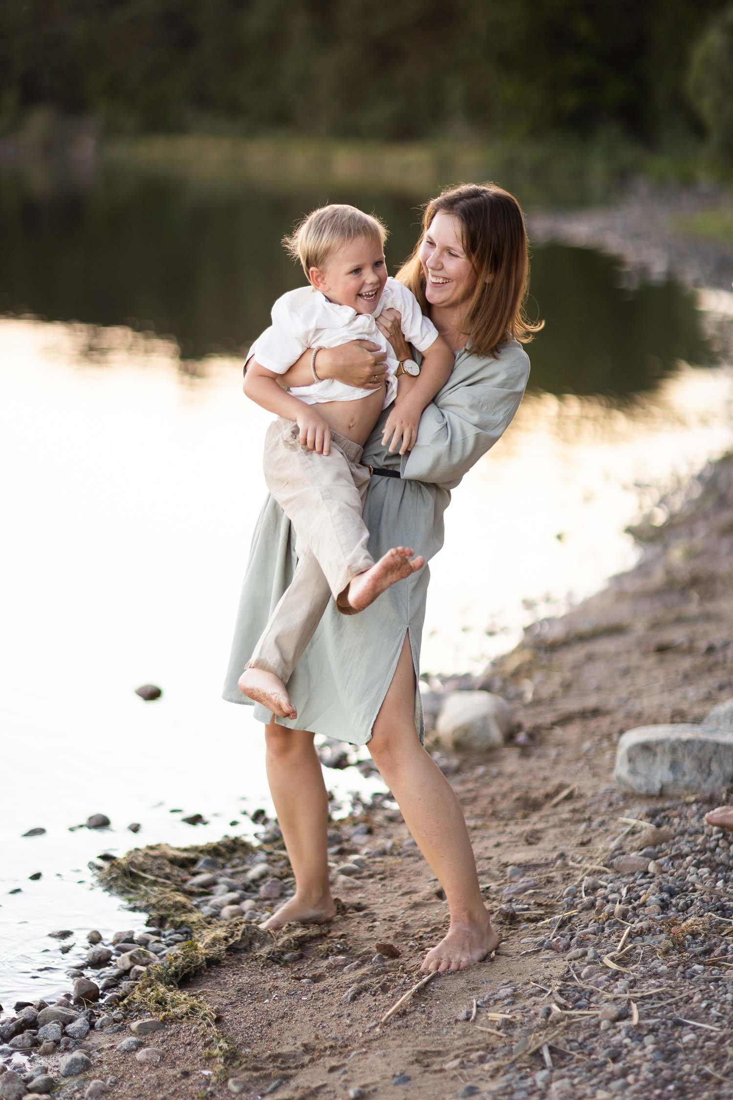 Mamma som busar med sin son nere vid vattnet på en strand i Linköping under en familjefotografering.