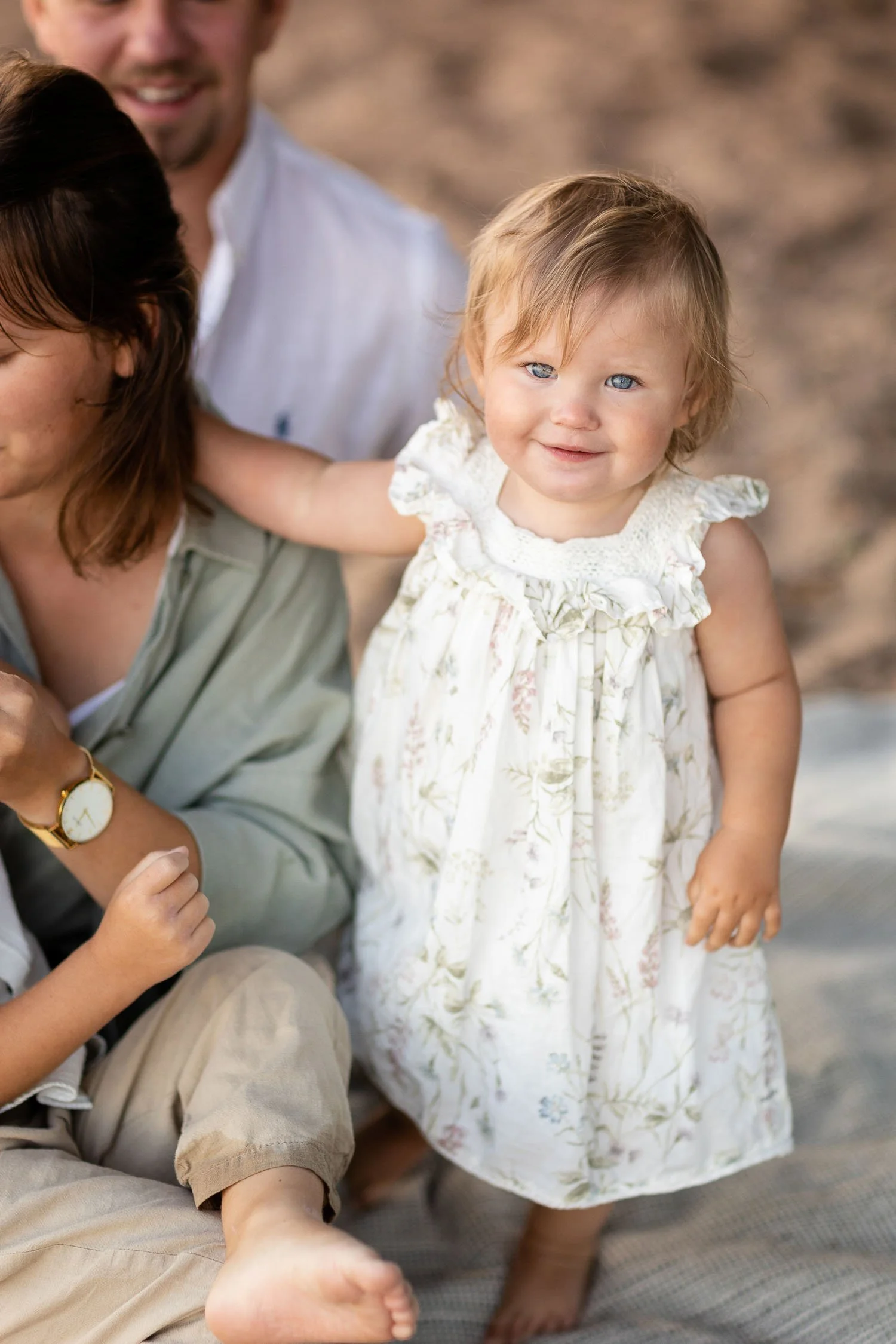 Lillasyster i familjen är nära mamma och ler stort in i kameran under fotograferingen i Linköping en varm magisk sommardag i augusti.