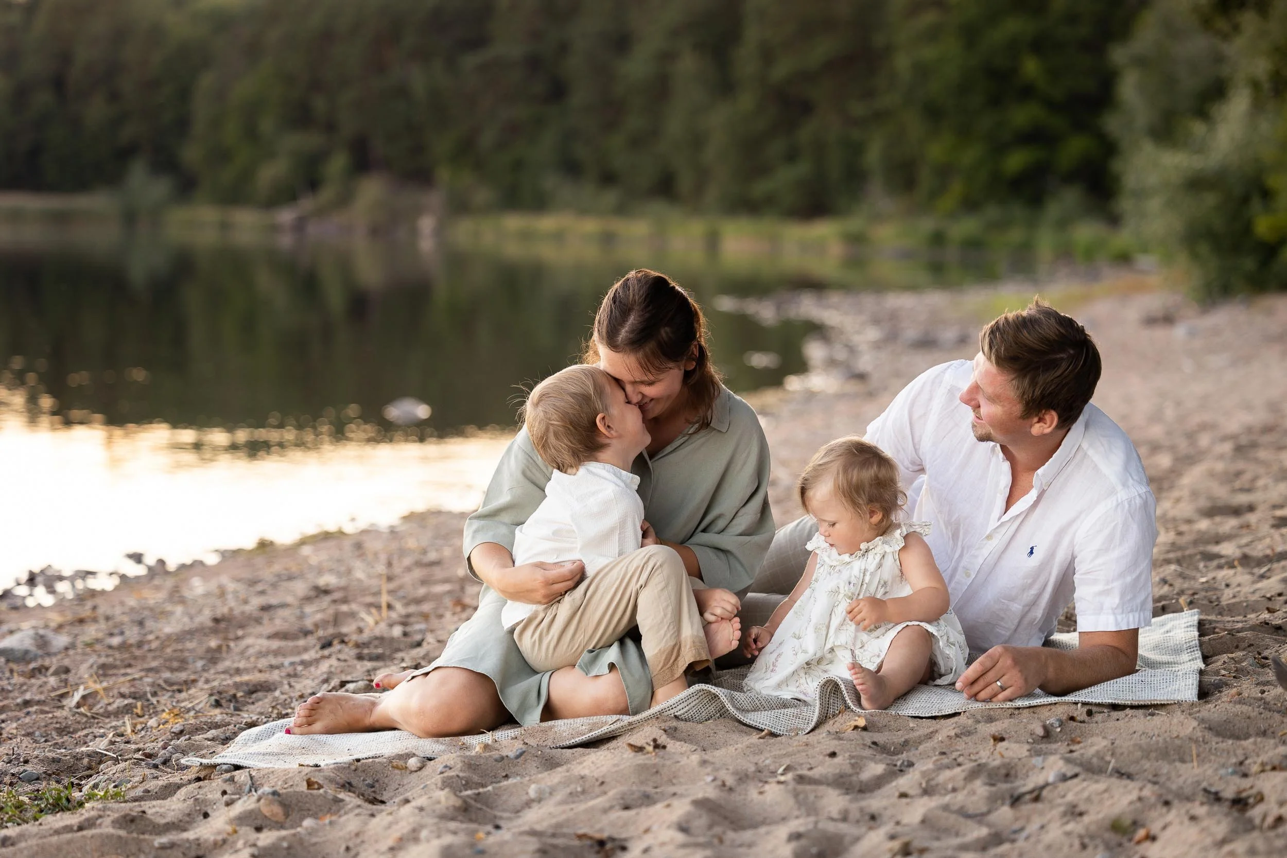 En strand och en picknickfilt i sanden med familjen mysandes tillsammans i det magiska fotoljuset. Familjefotografering i Linköping.