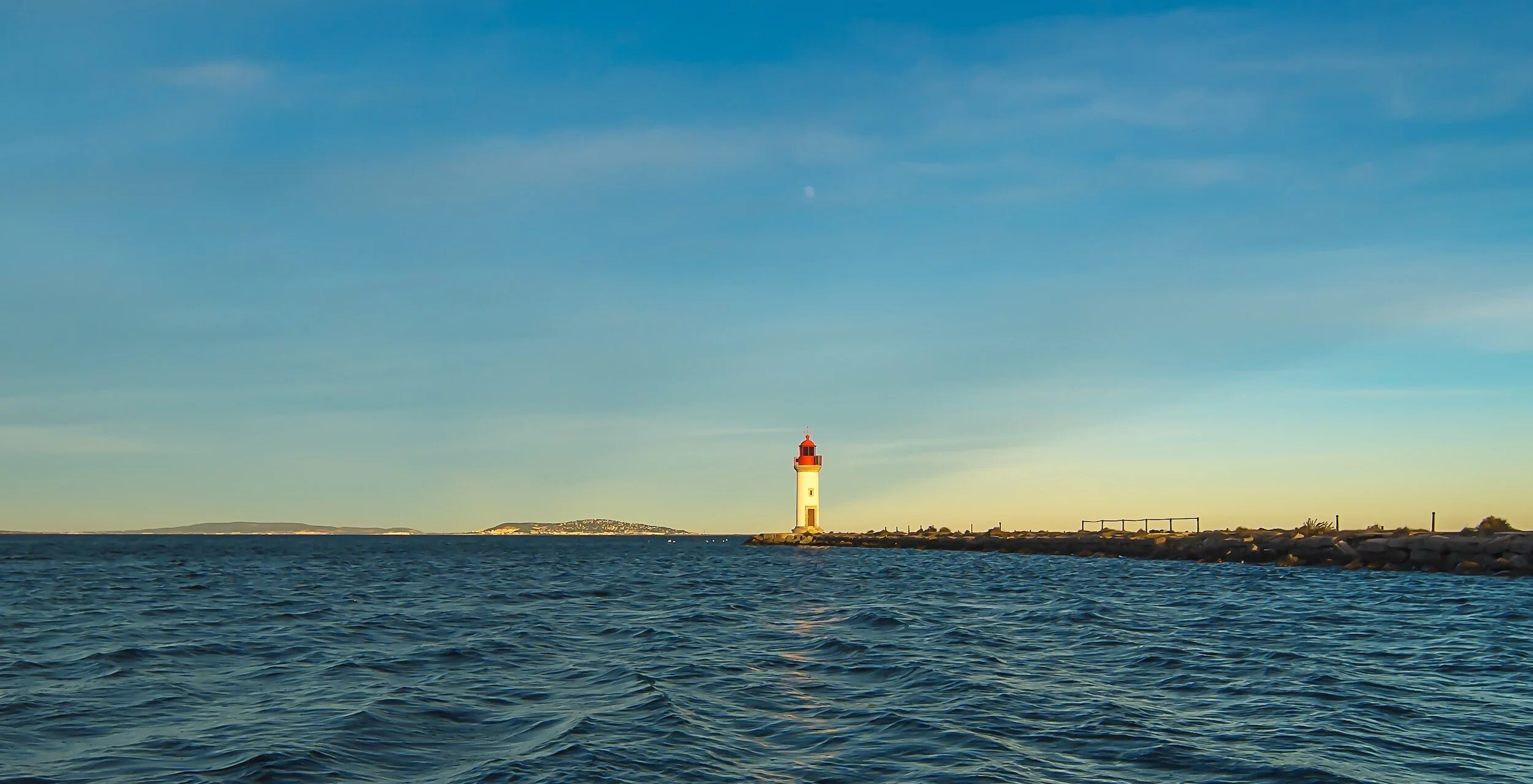 Phare au bord de la mer à l'heure dorée avec ciel dégagé.
