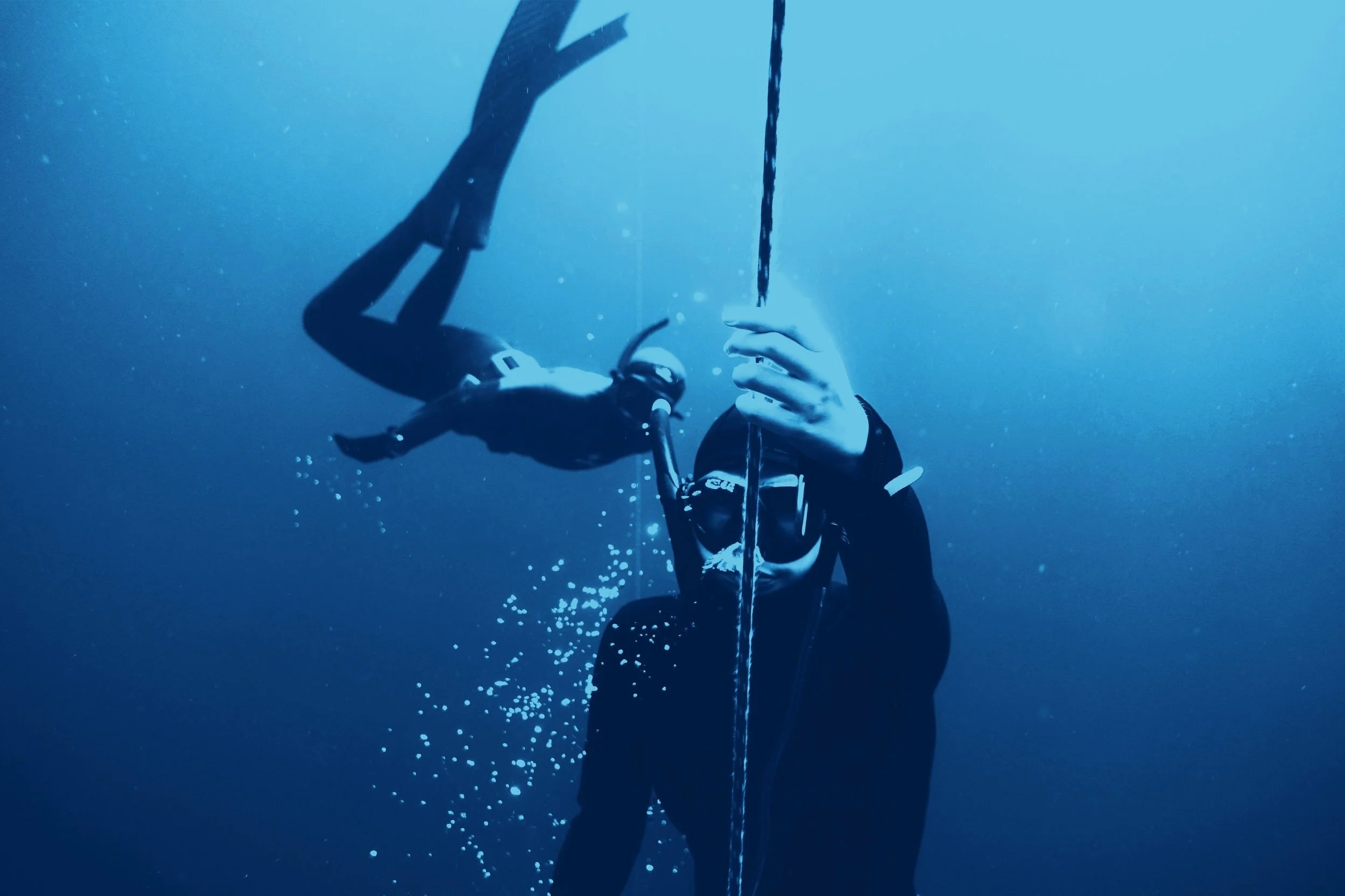 Deux plongeurs en apnée sous l'eau, tenant une corde, avec des bulles d'air autour d'eux.