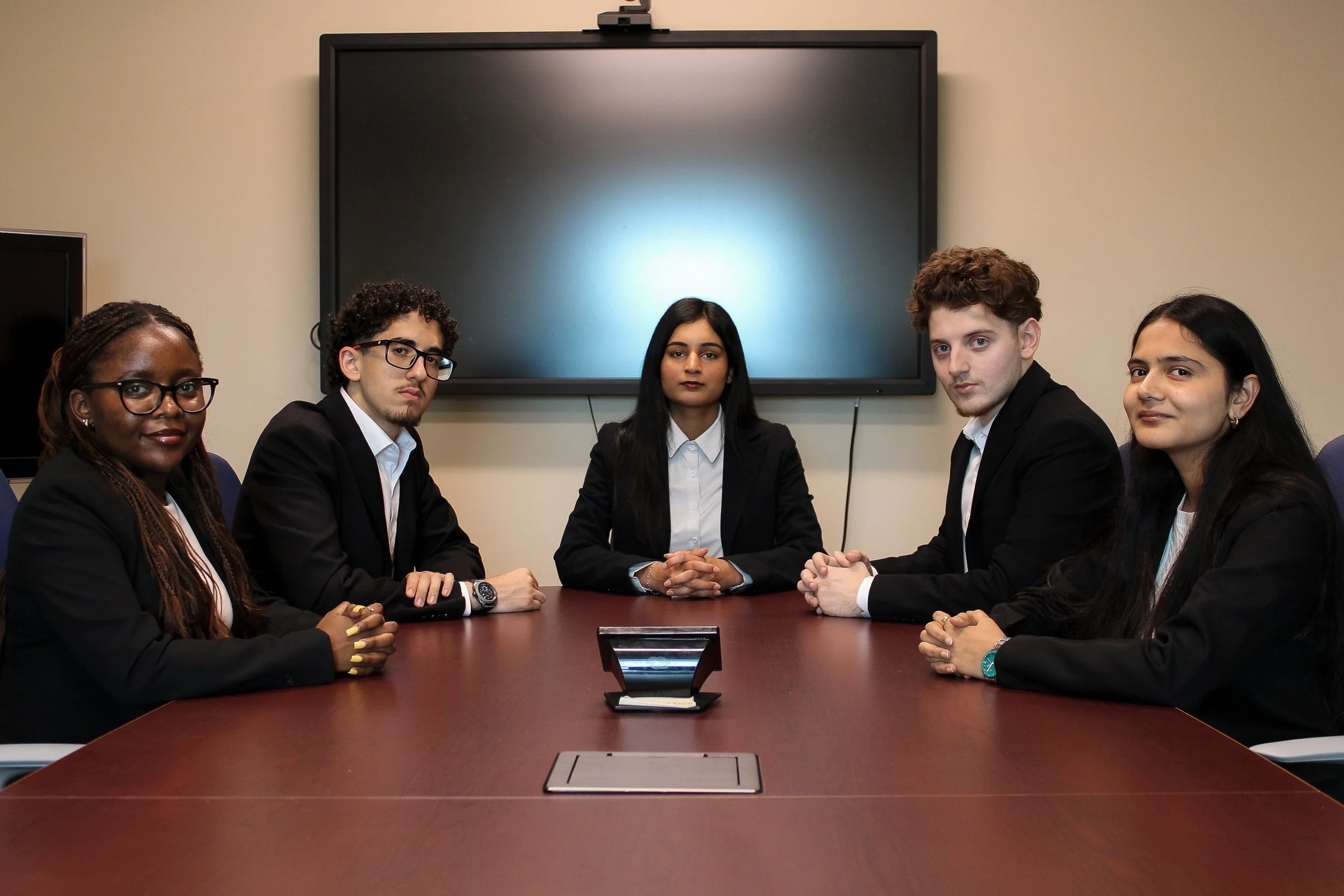 A group of six young adults, wearing matching maroon polo shirts with company logos, stand side by side in an office setting, smiling at the camera.