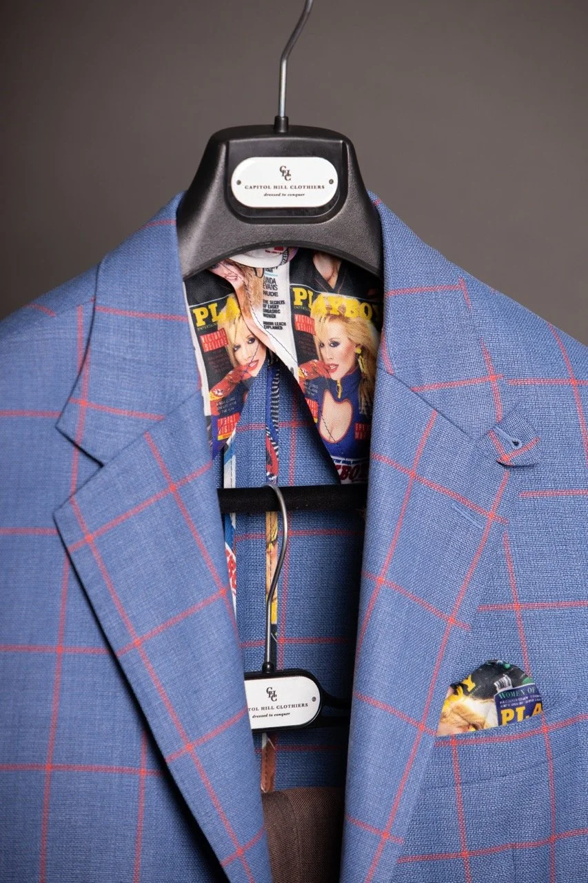 A blue plaid suit jacket with red lines on a hanger, featuring a lining with magazine covers. Fabrics for custom suits in Washington, DC