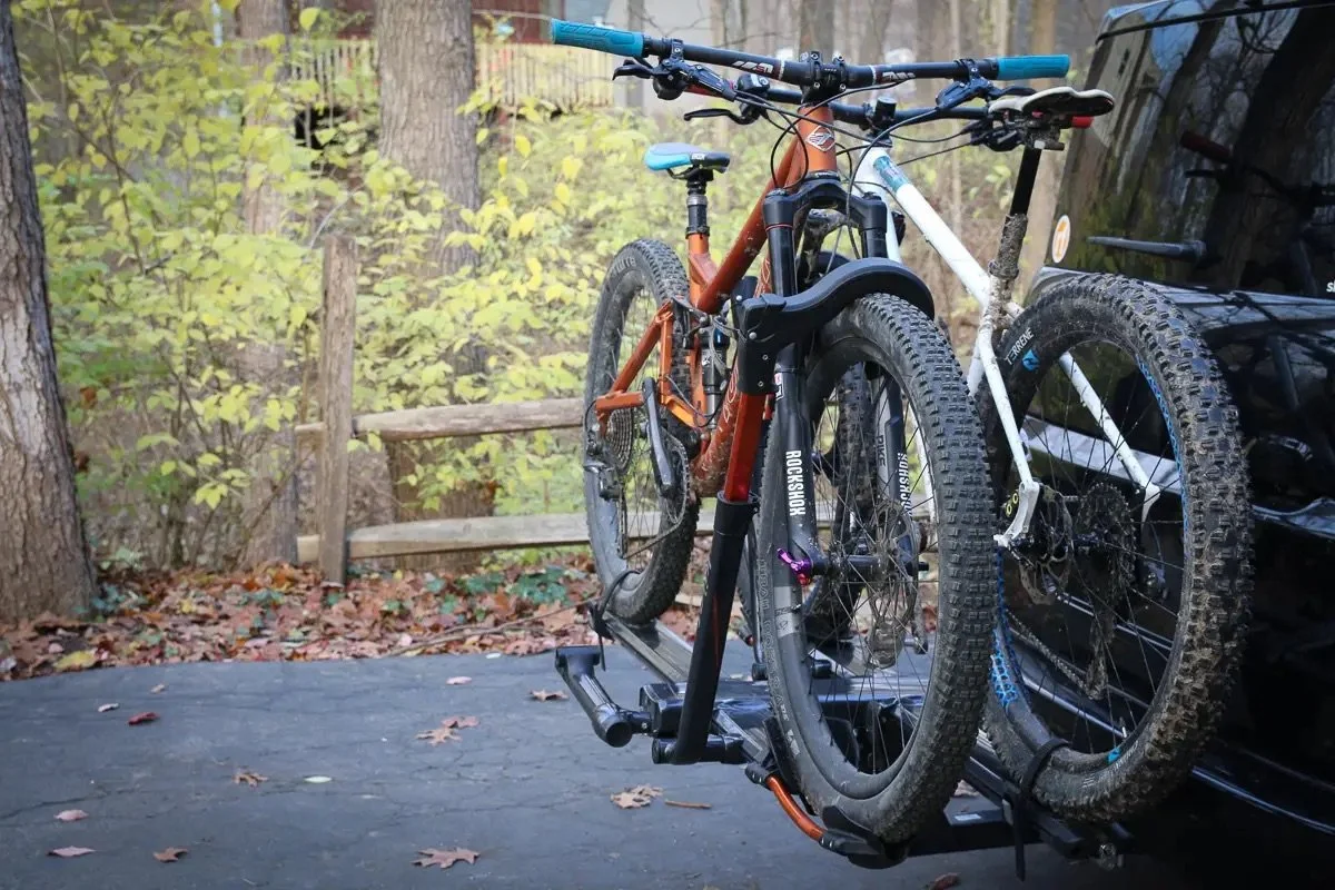 Twee mountainbikes op een fietsenrek achter een auto, in een bosrijke omgeving. Vandoya - outdoor - campers - vanlife - camper bouwen - camper huren - Merdeces Benz camper - 319 V6 4x4 -