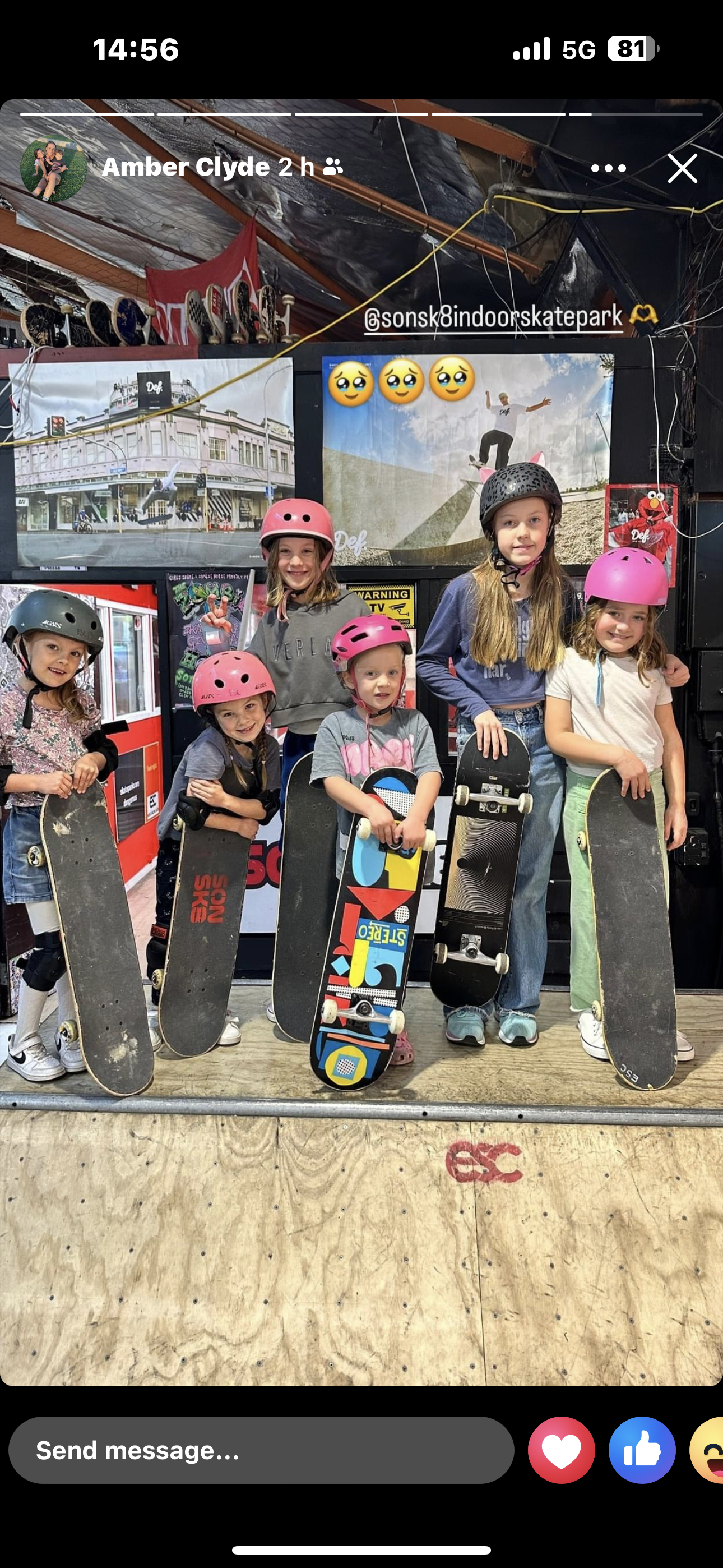 Group of young kids with helmets holding skateboards at an indoor skate park.