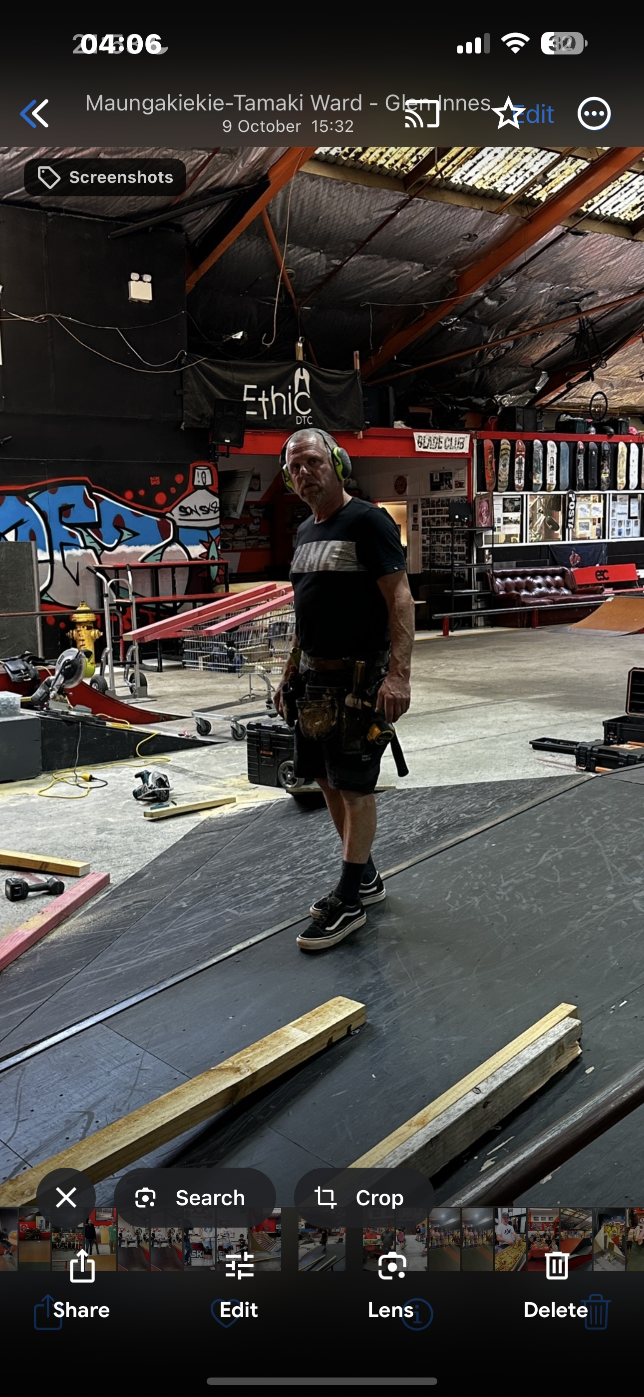 Man wearing protective earmuffs in a workshop with ramps, tools, and skateboard deck displays. Graffiti and Ethic DTC sign in background.