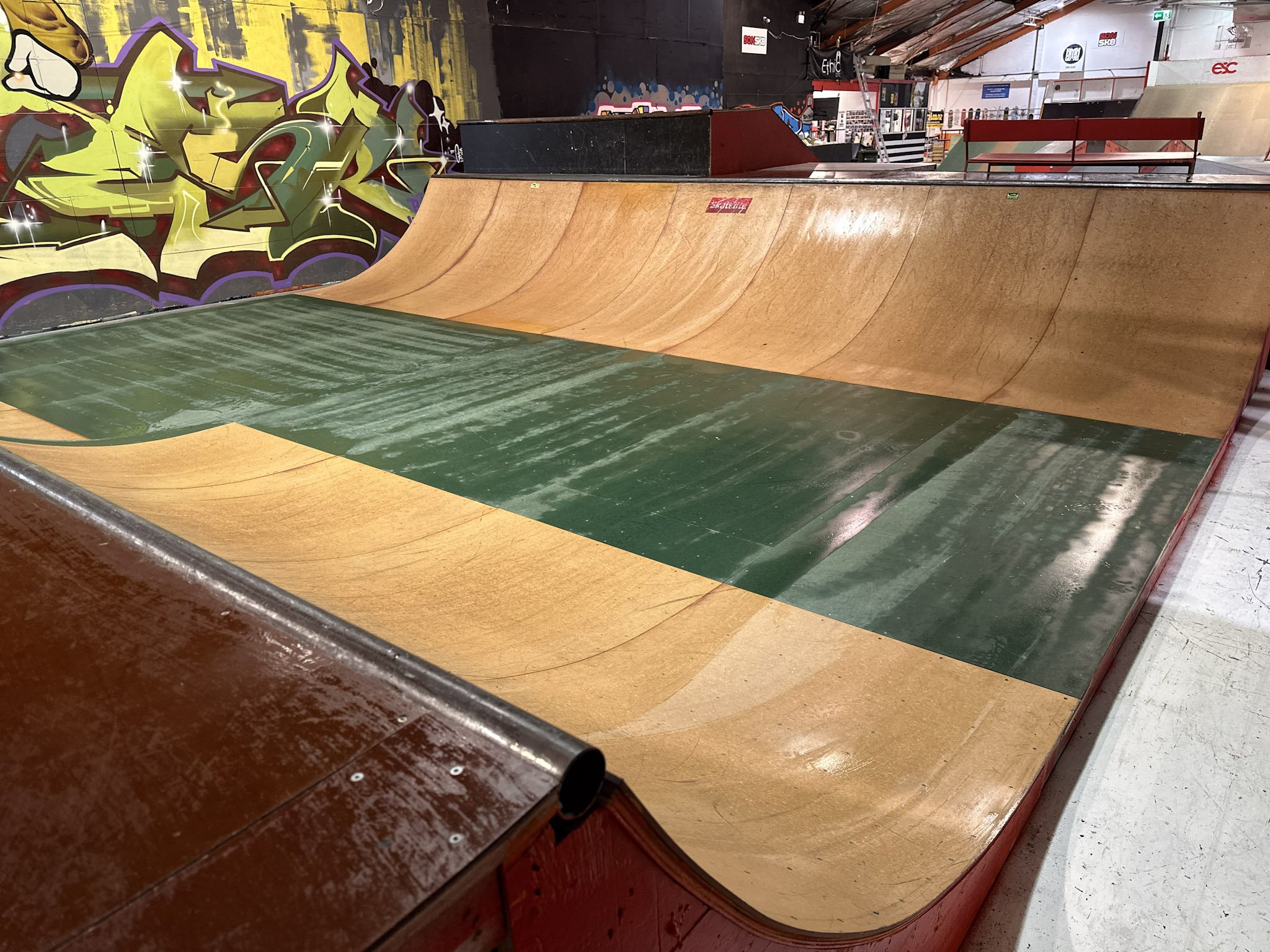 Indoor skatepark with a wooden halfpipe and colorful graffiti on the wall.