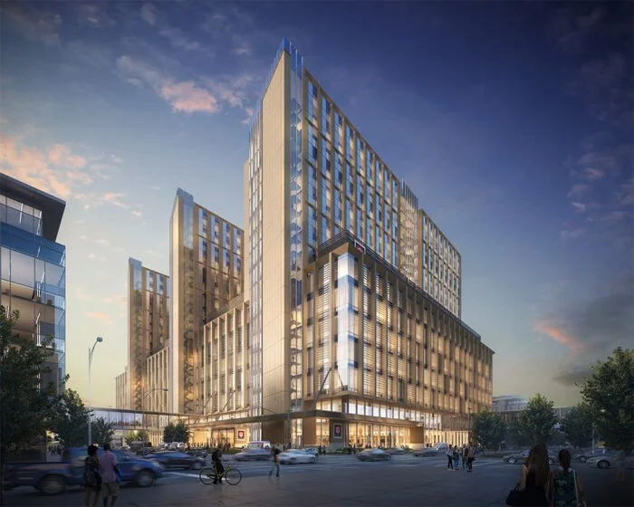 Modern high-rise building at sunset with glass facade and multiple floors, surrounded by cars and pedestrians.