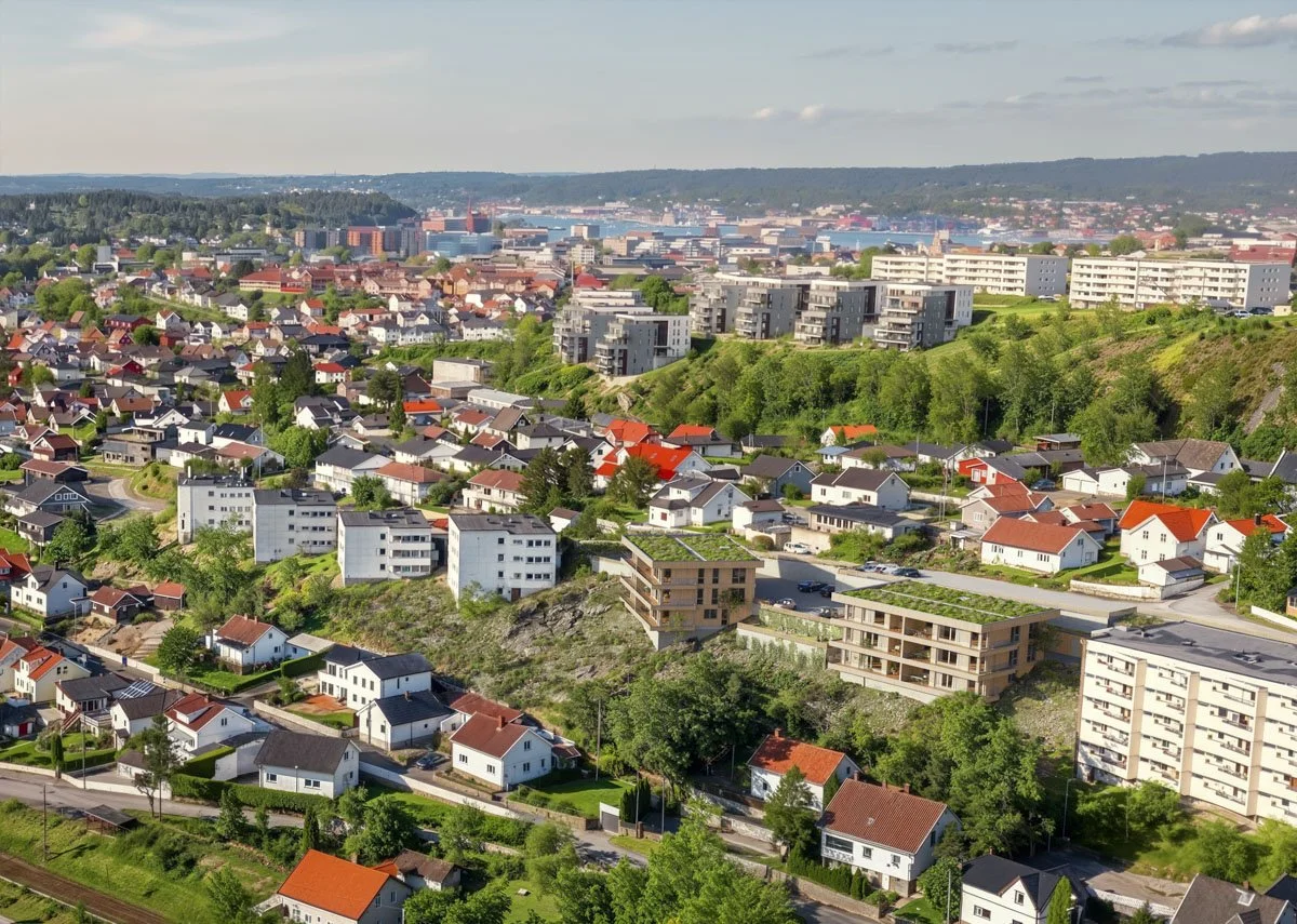 En byutsikt med boliger, grønne områder og et vann i bakgrunnen.