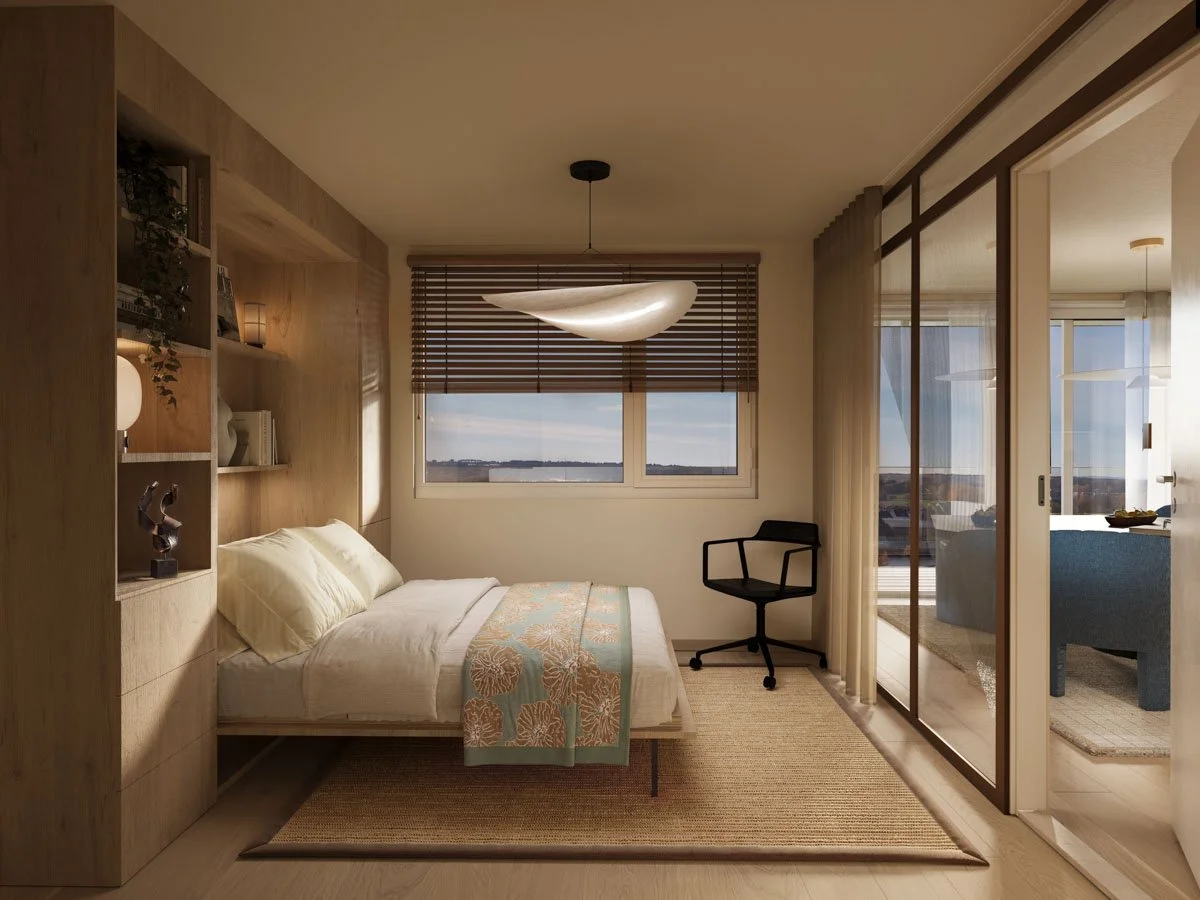 Et lyst og moderne soverom med seng, vindu med blinds, skrivebord med stol, og en romdeler som skiller soverommet fra stuen som har en blå lenestol og spisebord.