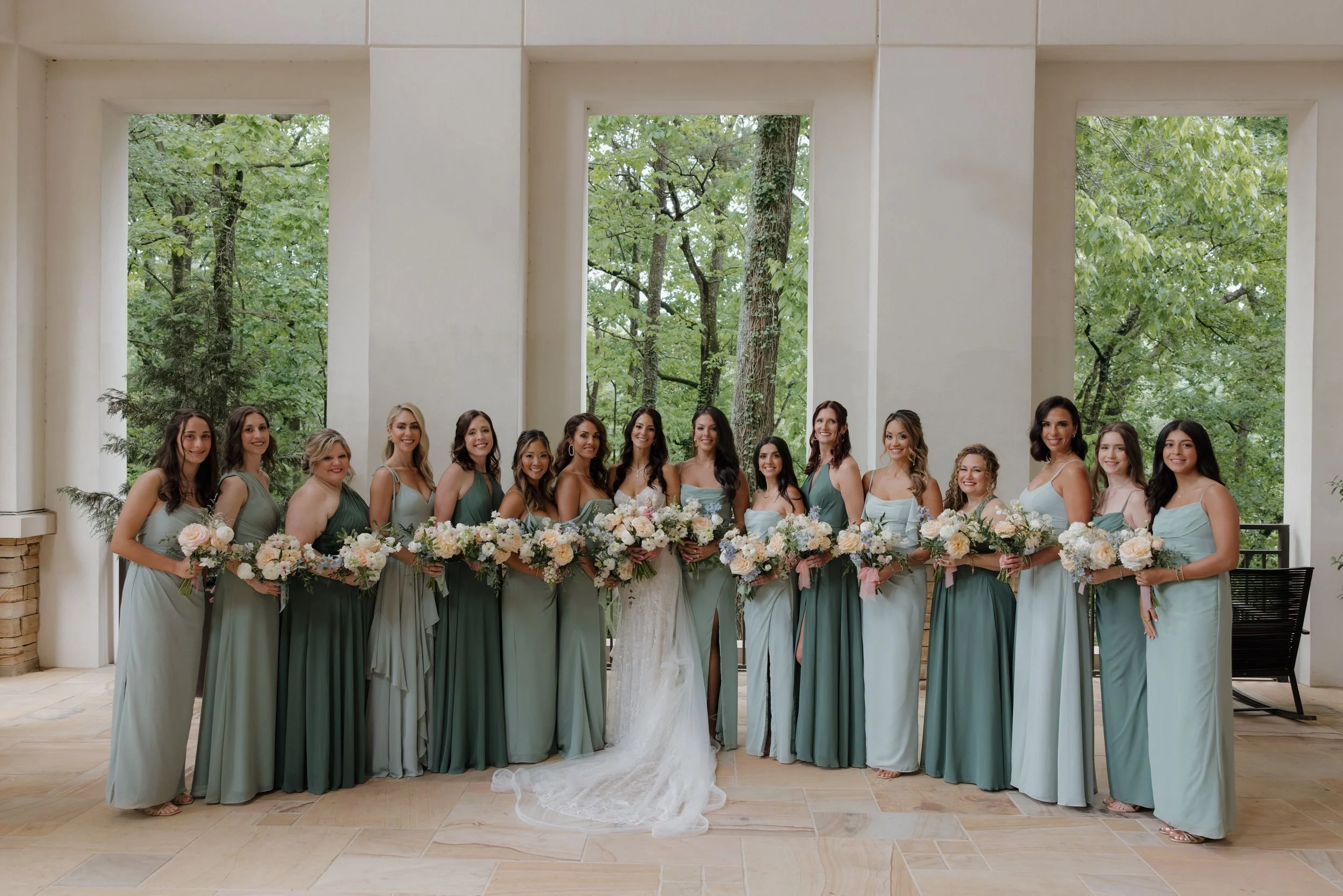 Bride with her bridesmaids in sage dresses holding ivory and blush bouquets on a columned veranda