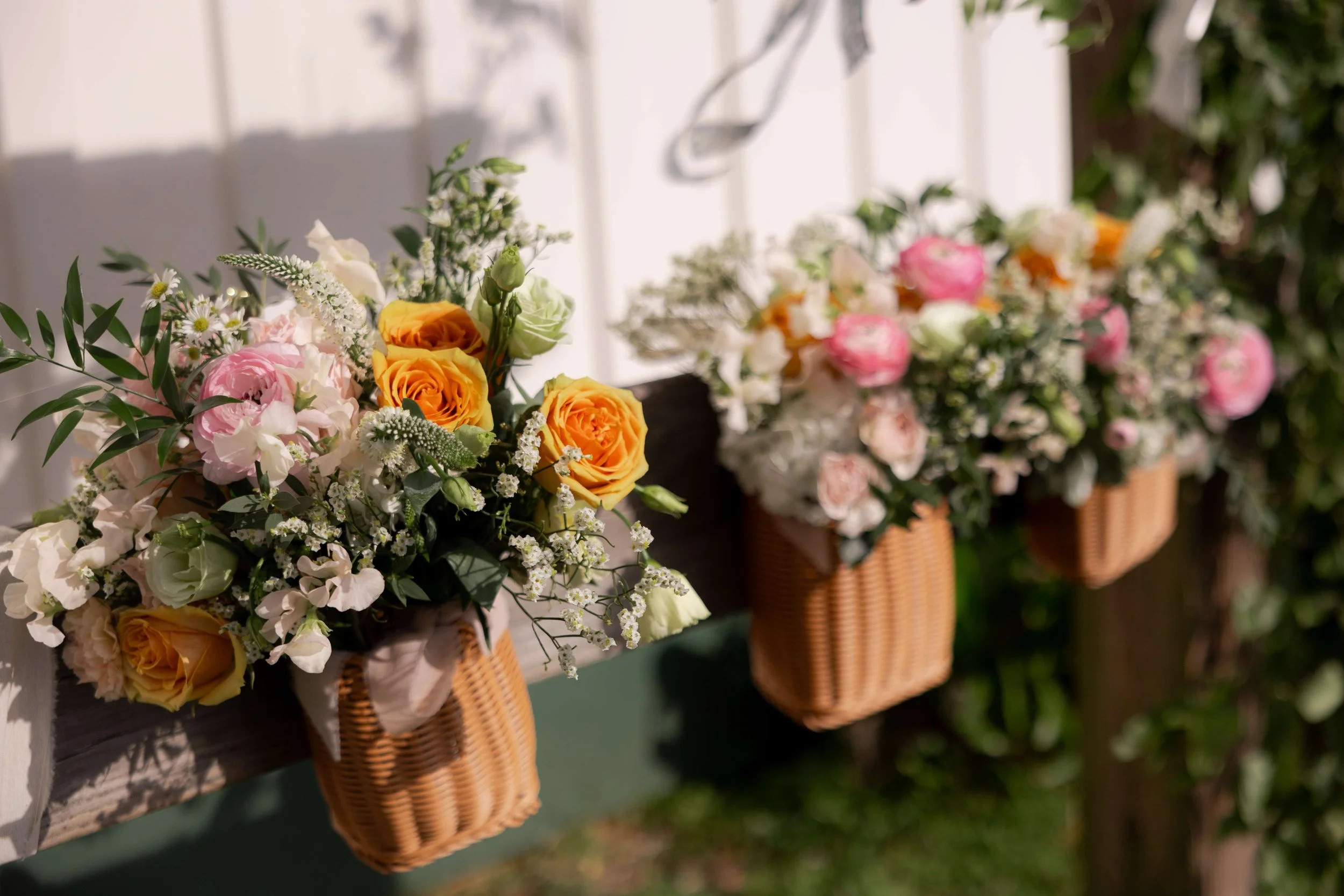 Colorful spring wedding floral arrangements featuring orange roses, pink peonies, and greenery in rustic wooden baskets at Wild Daisy Farm venue in Georgia