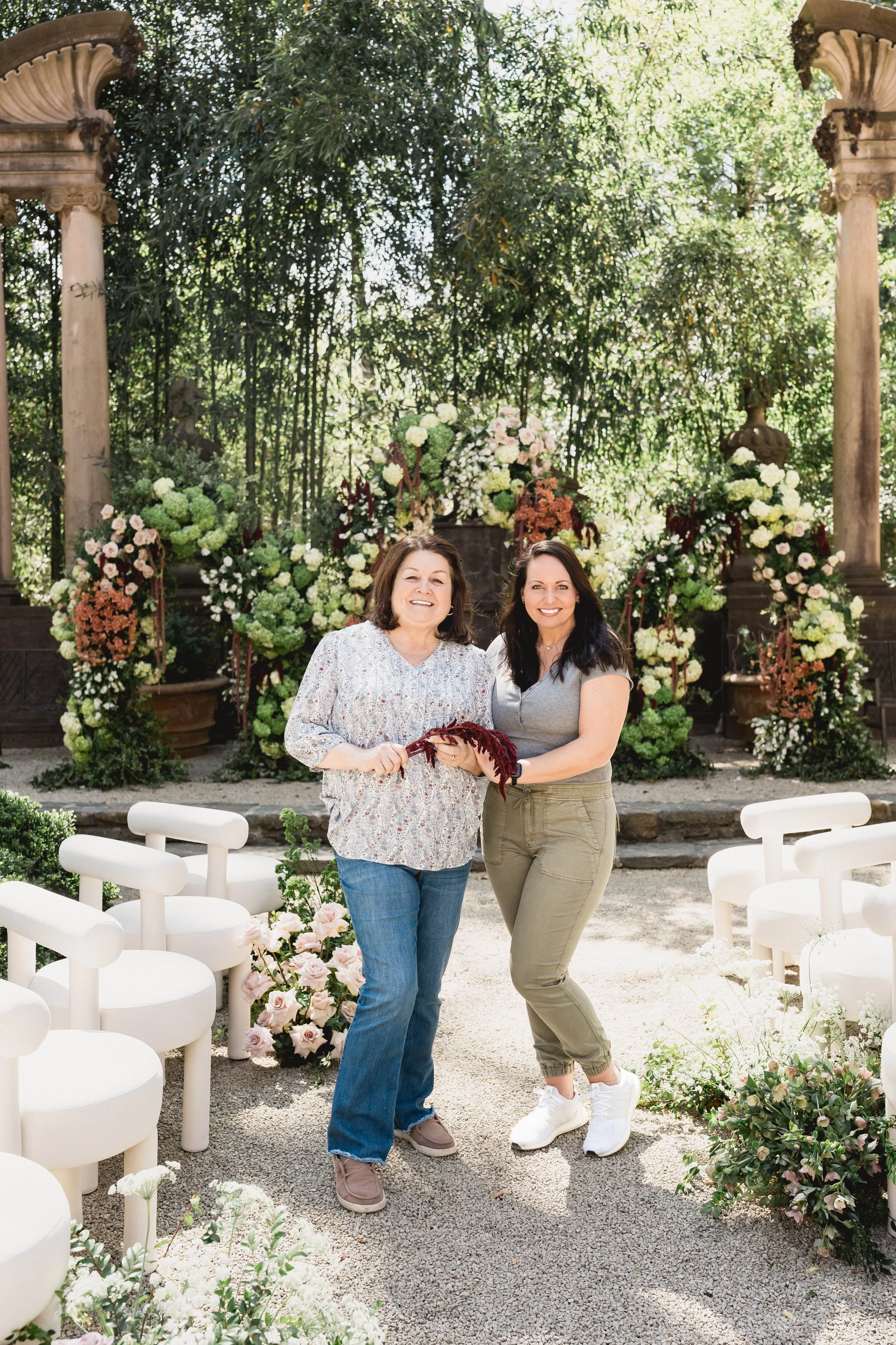 Flori Weddings floral designers at an estate ceremony with hydrangea, rose, and amaranthus arrangements under classical stone columns