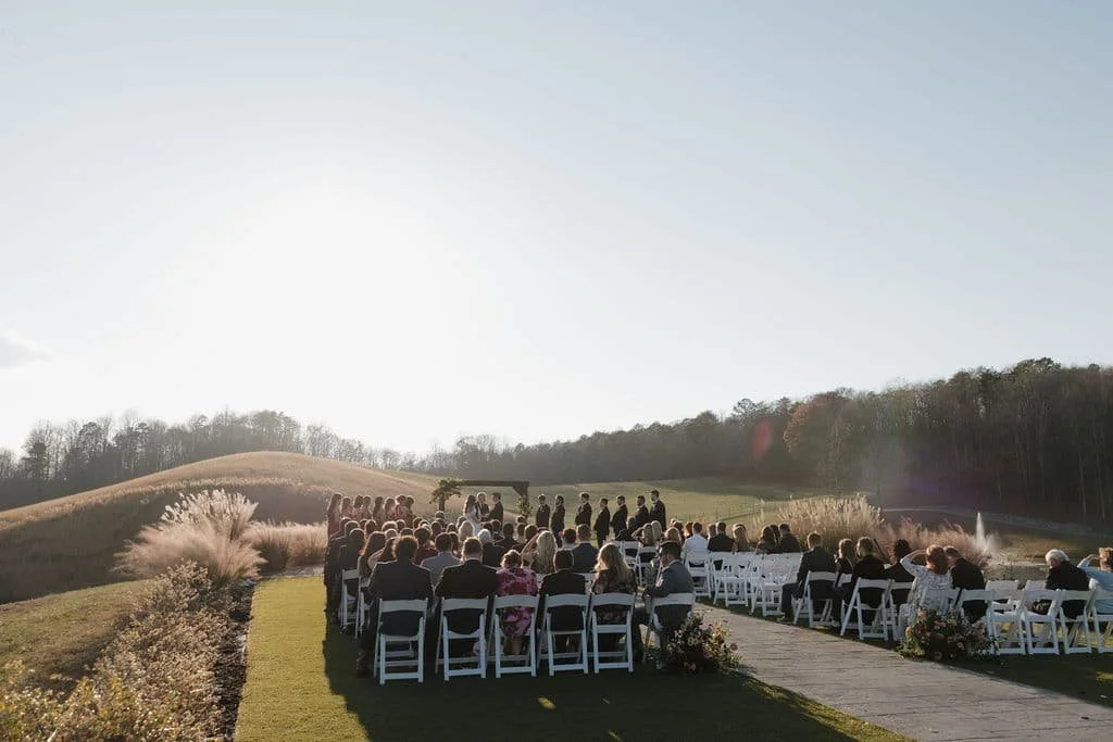 Outdoor wedding ceremony at Swan Lake Overlook in Dawsonville, Georgia with guests seated in white chairs on a hilltop overlooking the North Georgia mountains