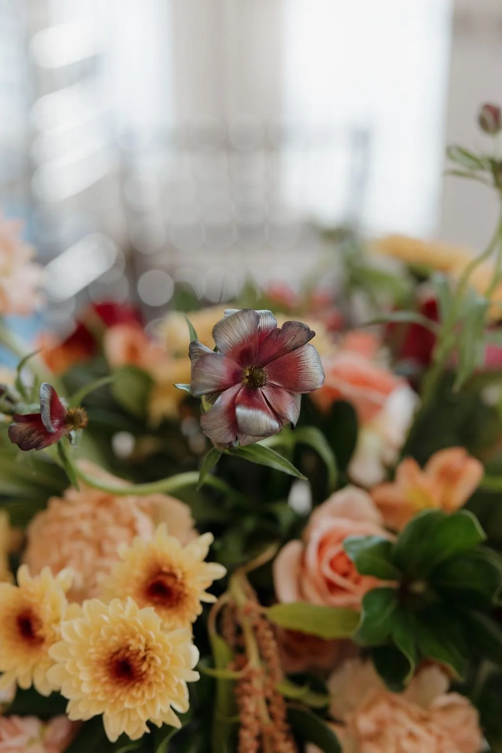 Close-up of a floral arrangement with yellow dahlias, peach roses, and a burgundy bloom